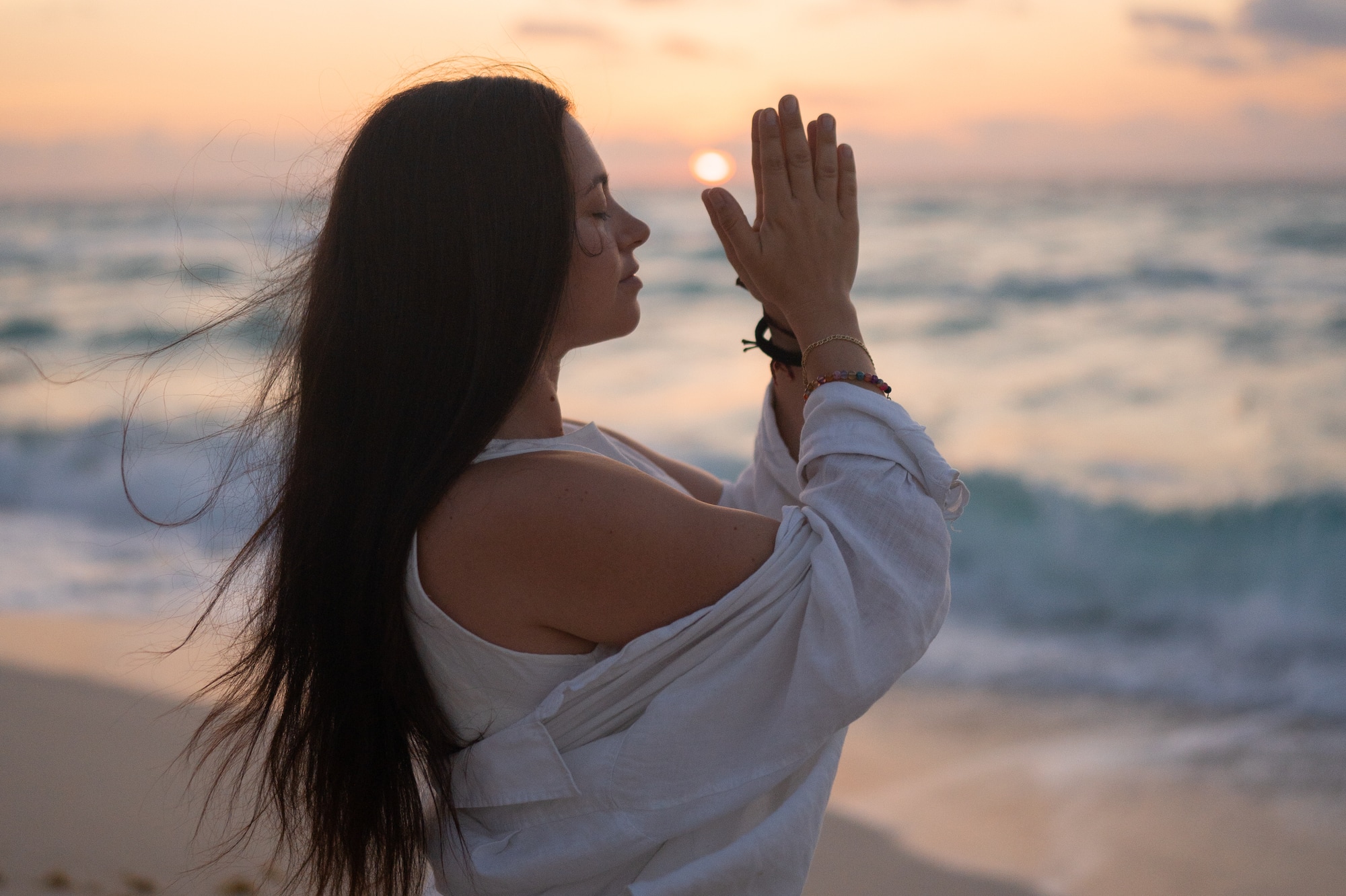 a woman standing on a beach with her hands together