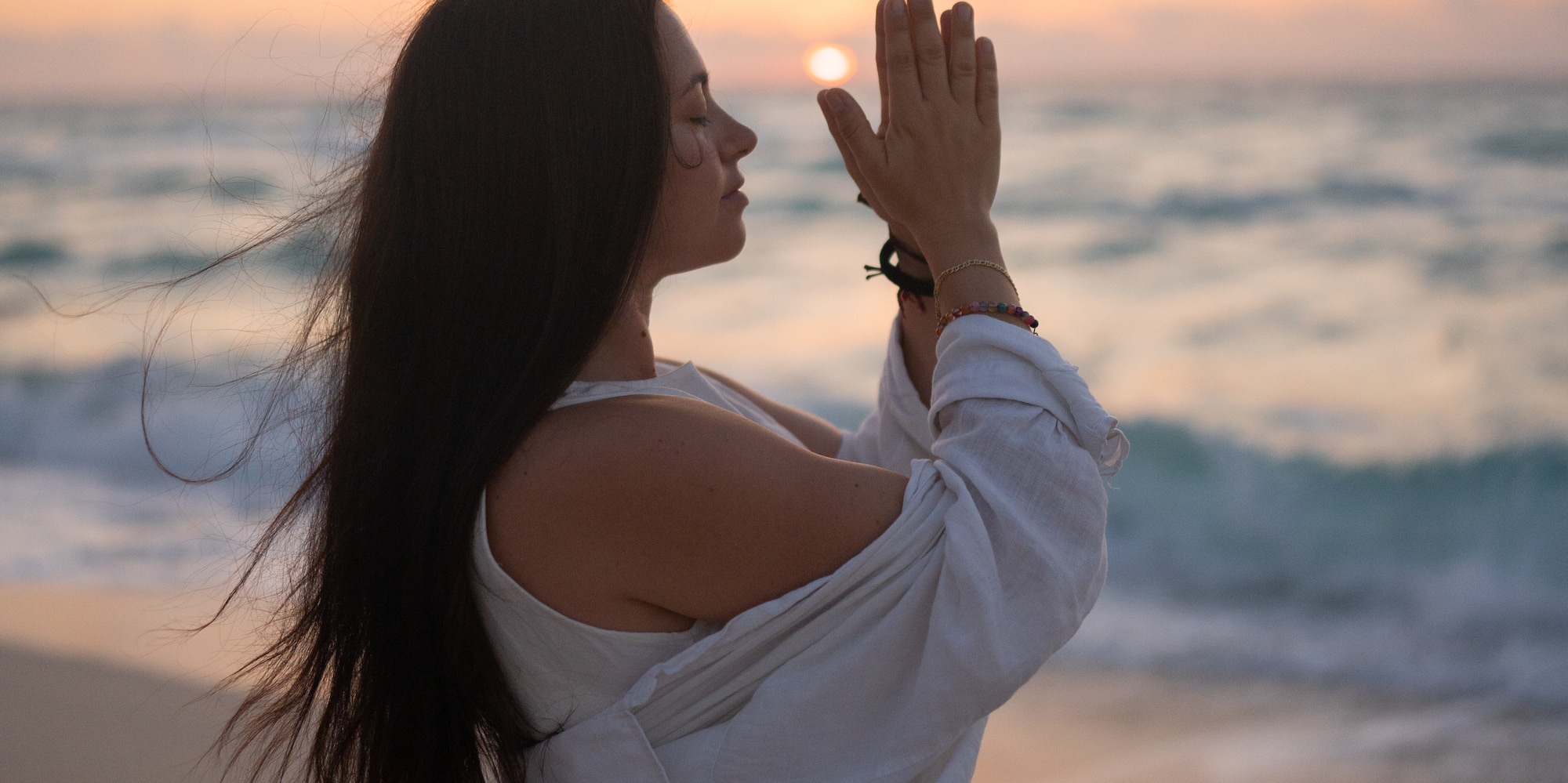 a woman standing on a beach with her hands together