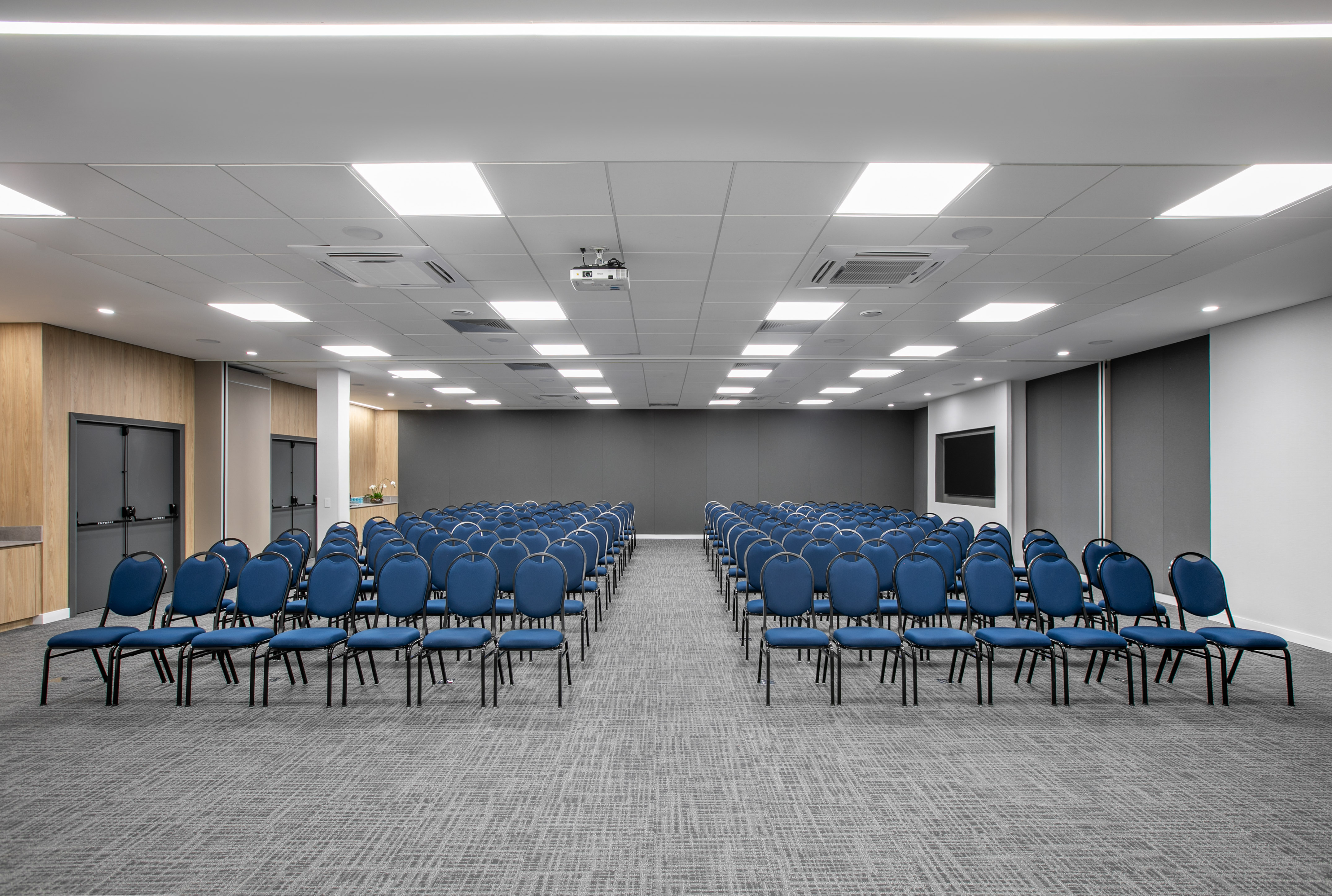 Empty conference room with blue chairs, projector, and screen.