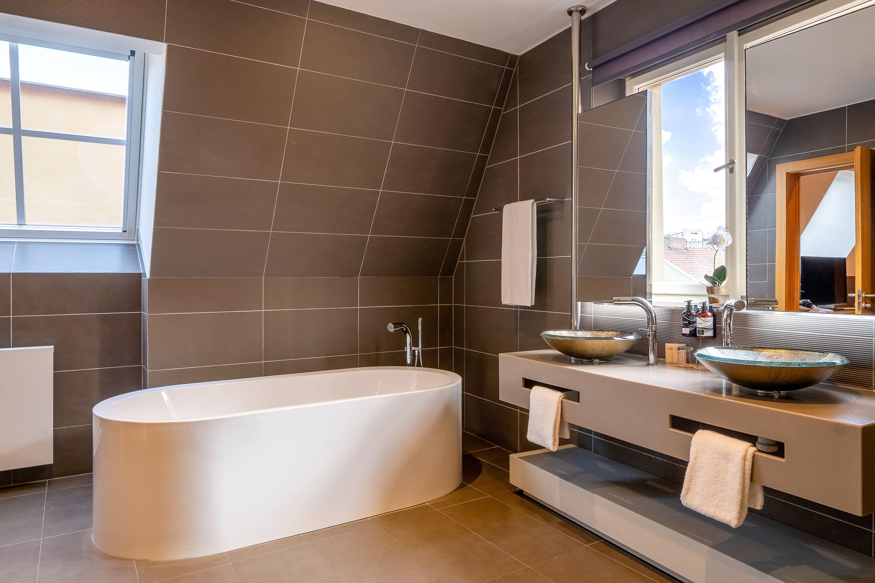 Stylish attic bathroom with freestanding bathtub, dual glass vessel sinks.