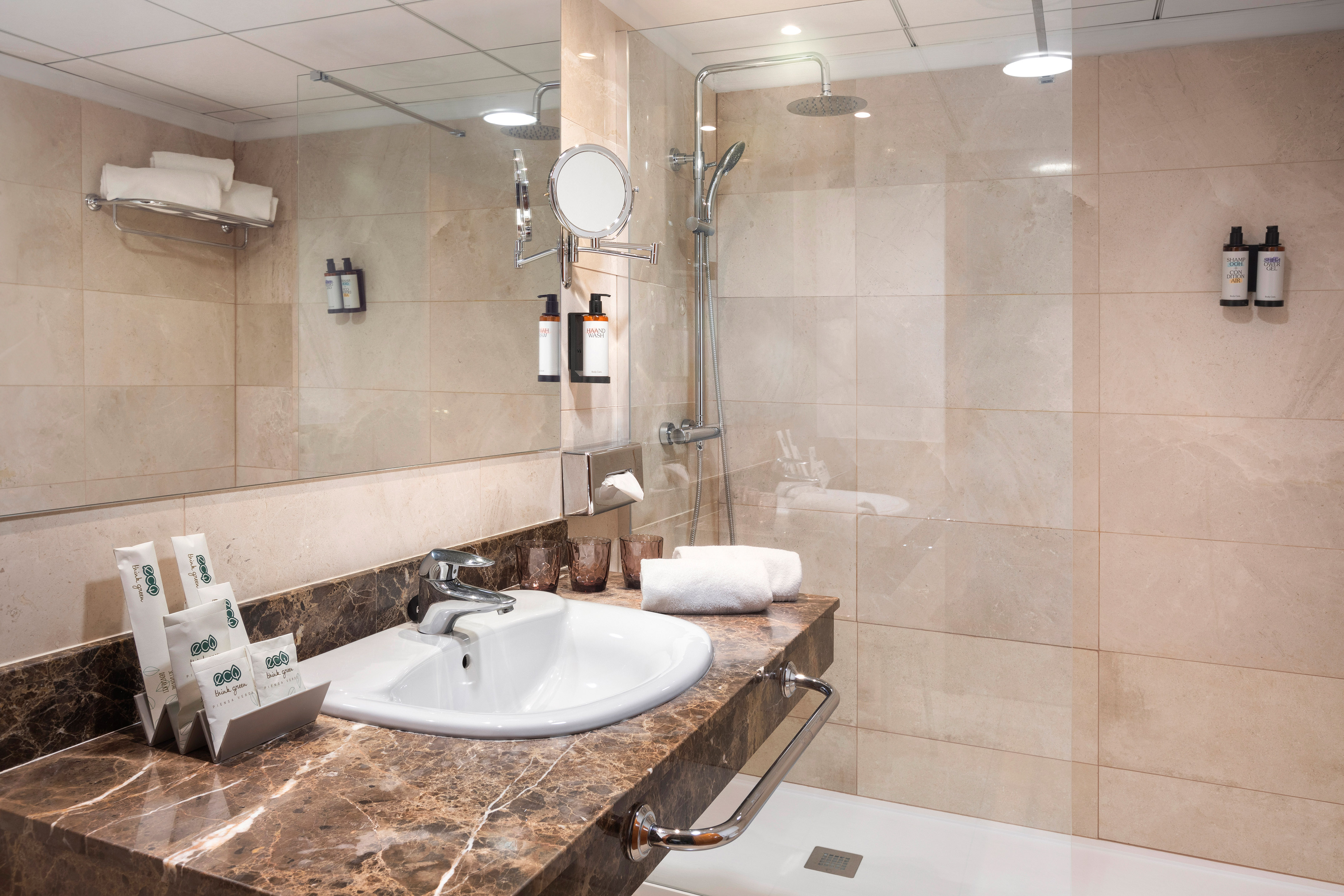 Modern hotel bathroom with marble vanity, sink, shower, and various hotel amenities.