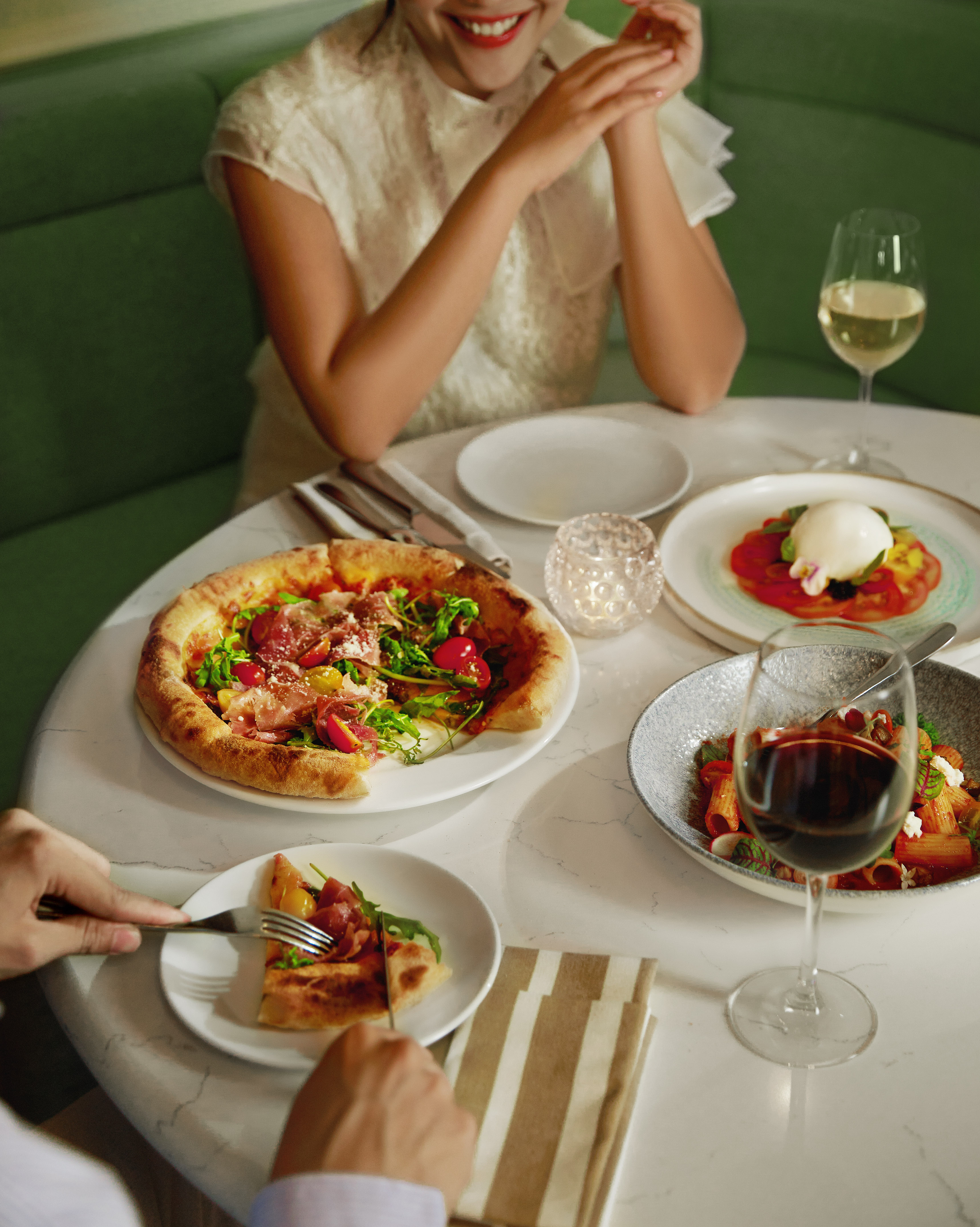 Couple enjoying Italian dinner: pizza, pasta, caprese salad, and wine.