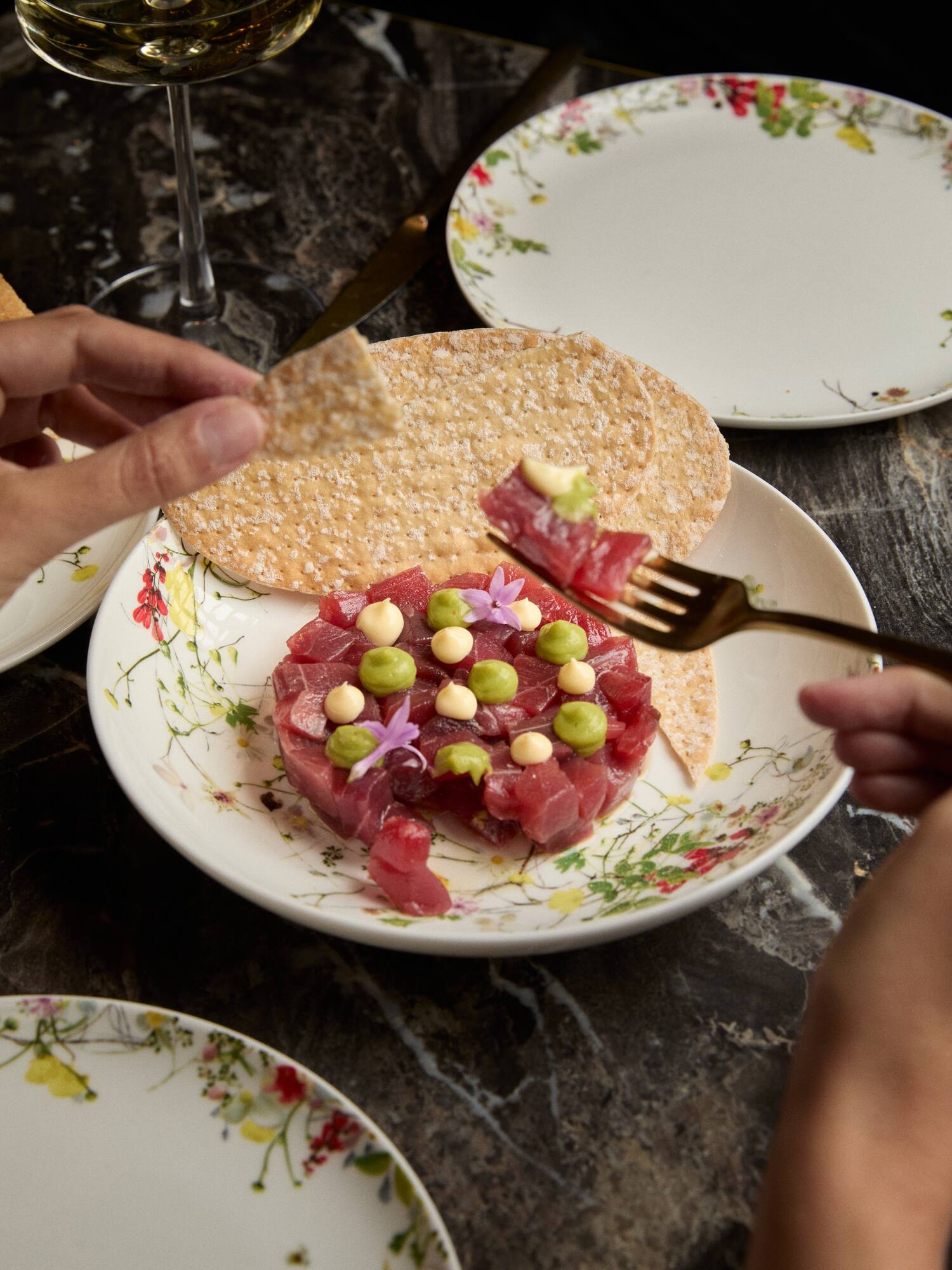 Tuna tartare with peas, sauce, edible flowers, and crackers on a floral plate.