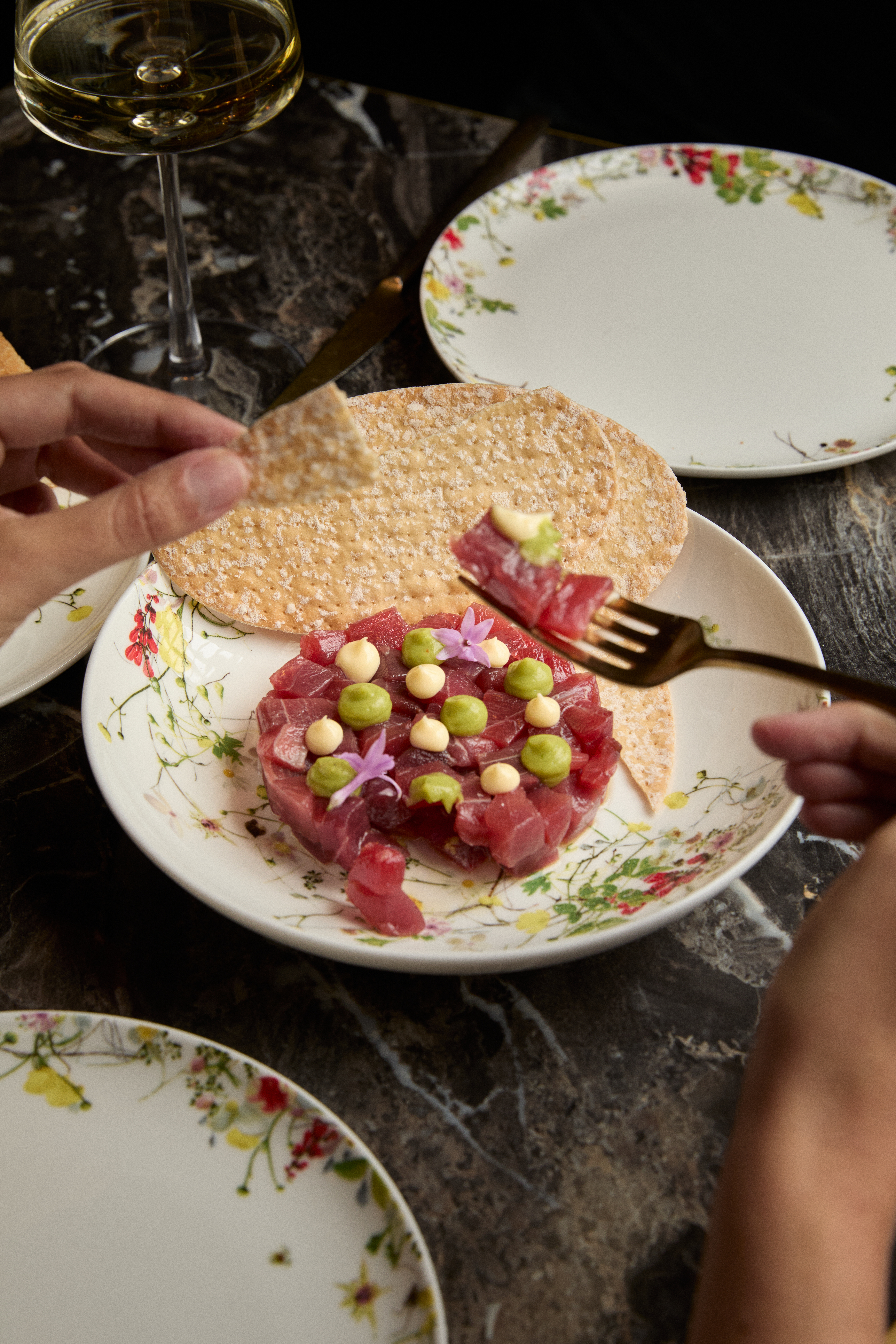 Tuna tartare with peas, sauce, edible flowers, and crackers on a floral plate.