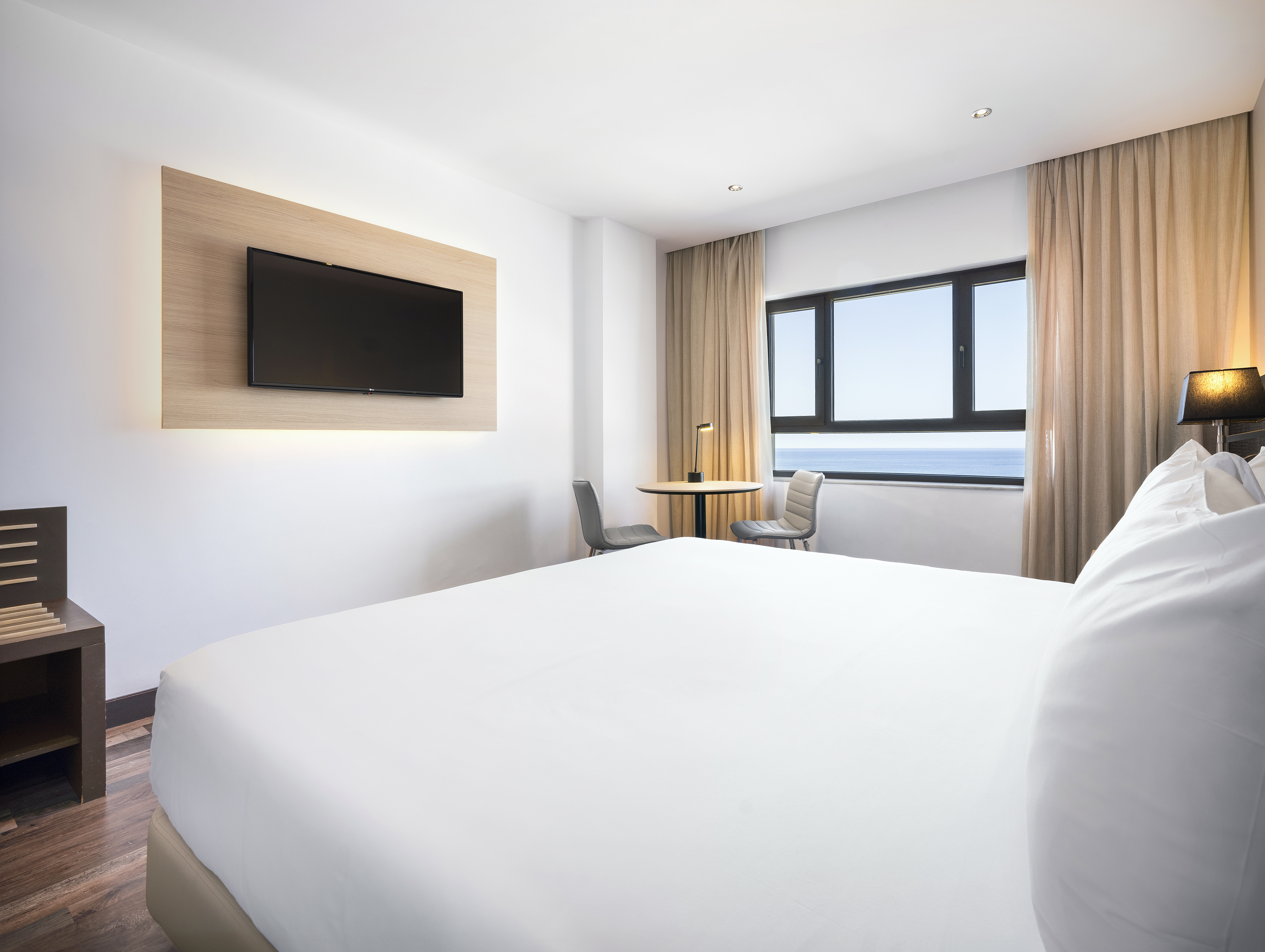 Modern hotel room with sea view, large bed, and wall-mounted TV.