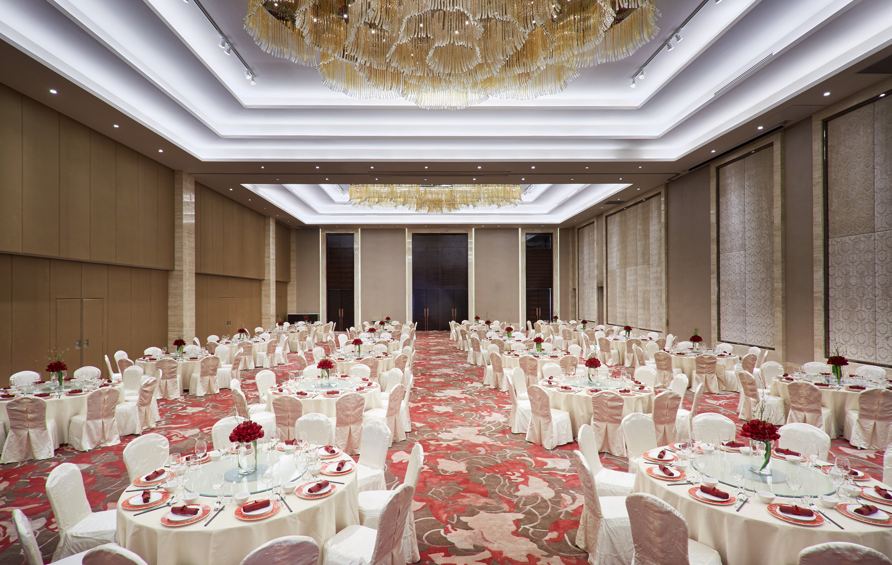 Elegant banquet hall with dining tables, red decor, and large chandeliers.
