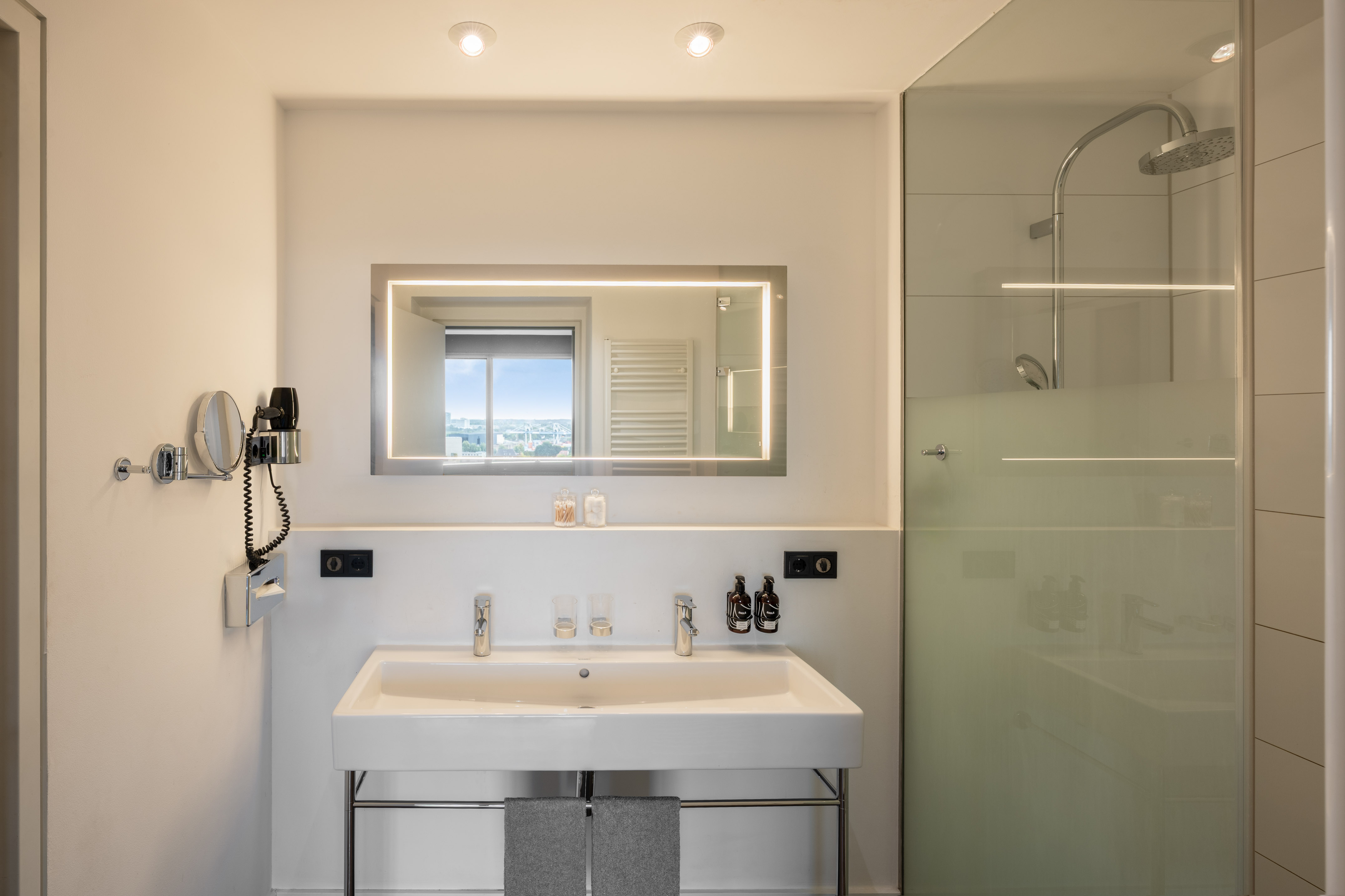 Modern bathroom with double vanity, illuminated mirror, and glass shower.