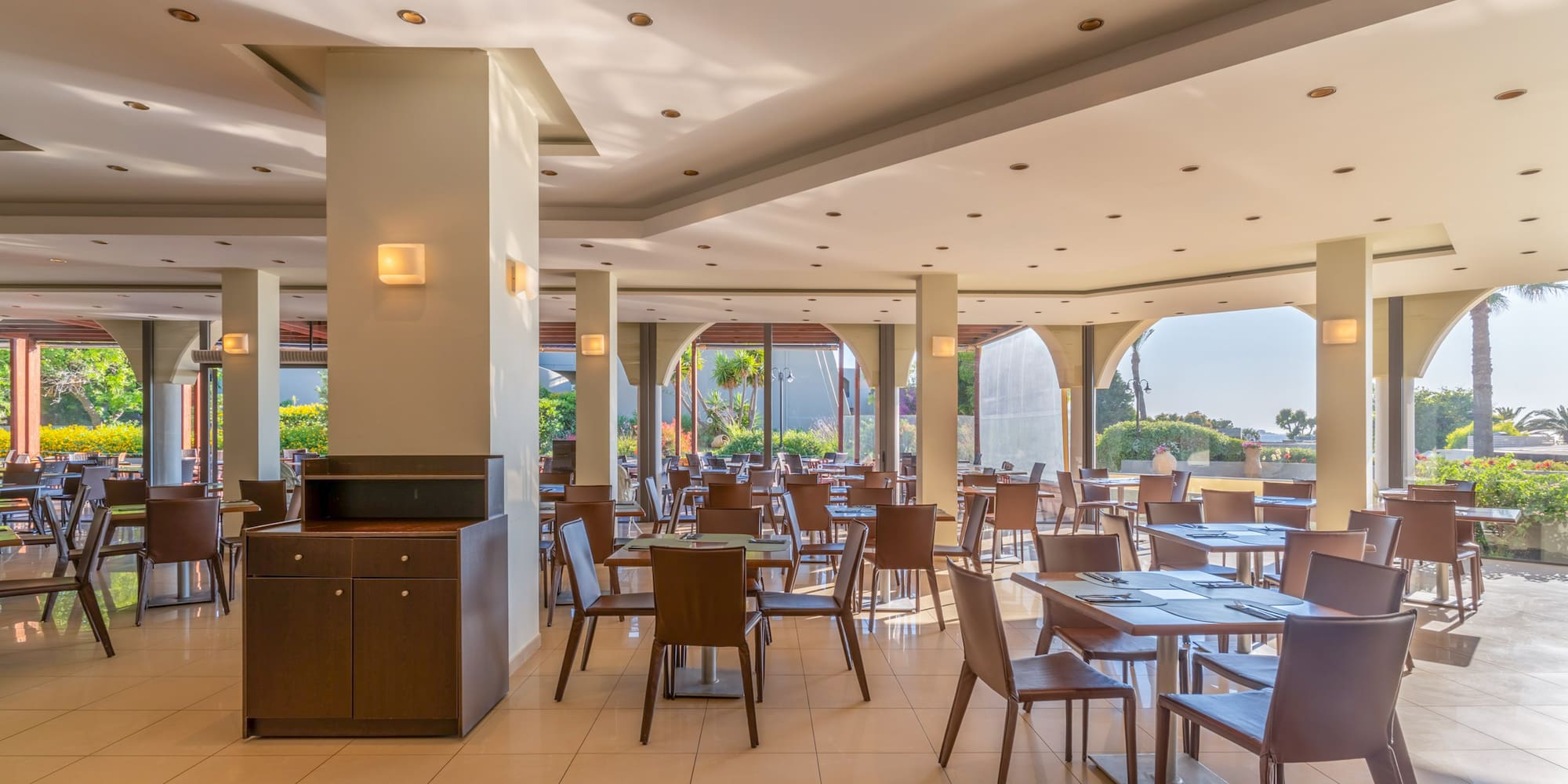 Modern resort restaurant with tables, chairs, and bright garden views.