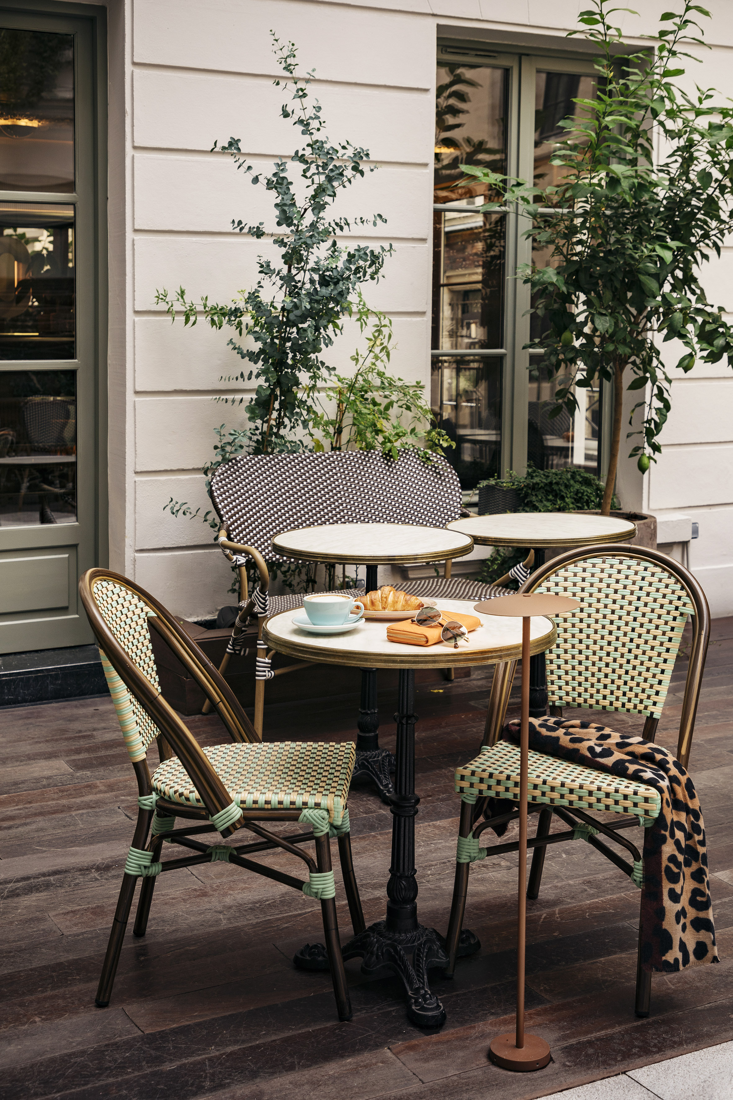 Parisian bistro cafe with woven rattan chairs, marble tables, coffee, and croissant.