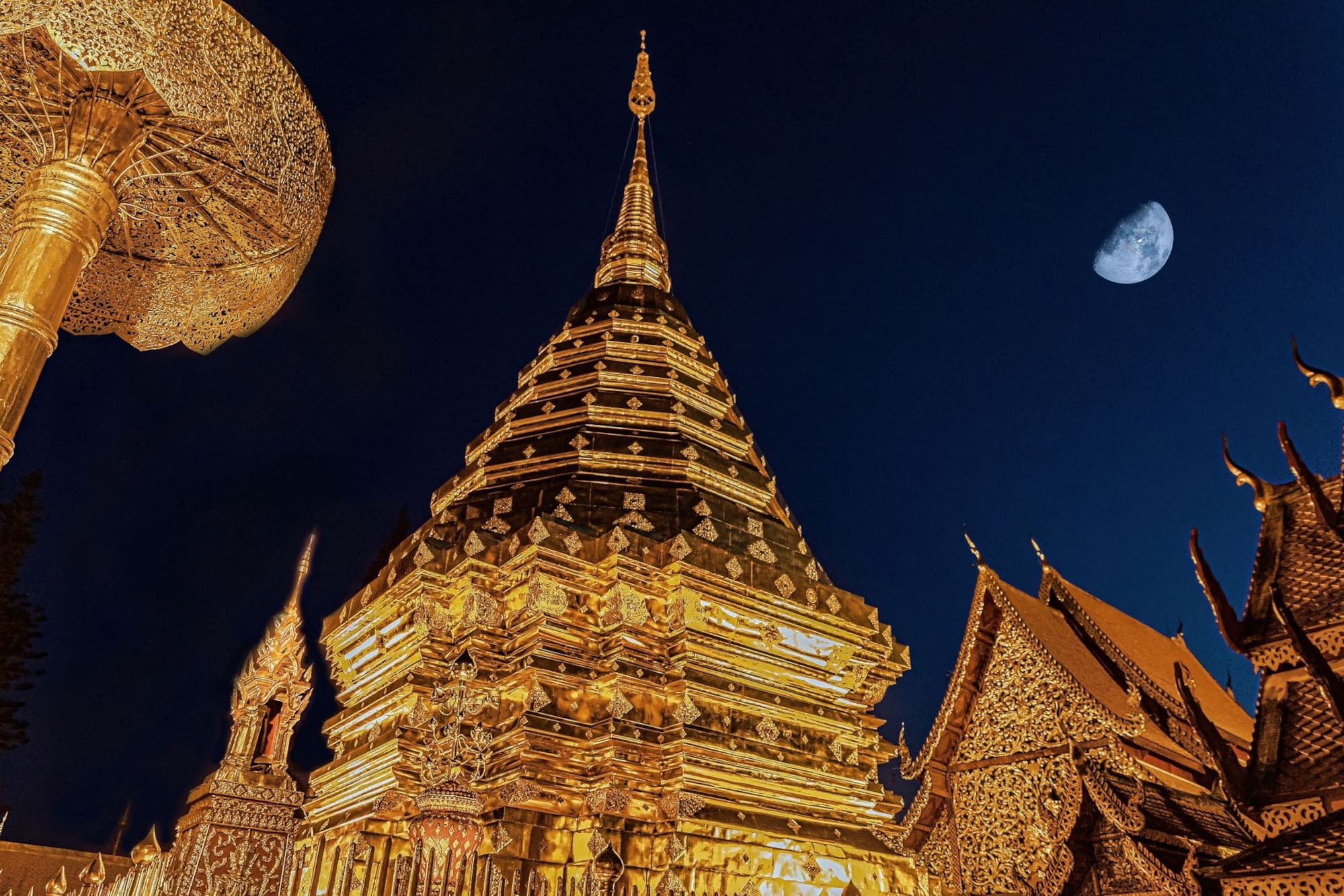 Golden Wat Phra That Doi Suthep pagoda illuminated at night with crescent moon.