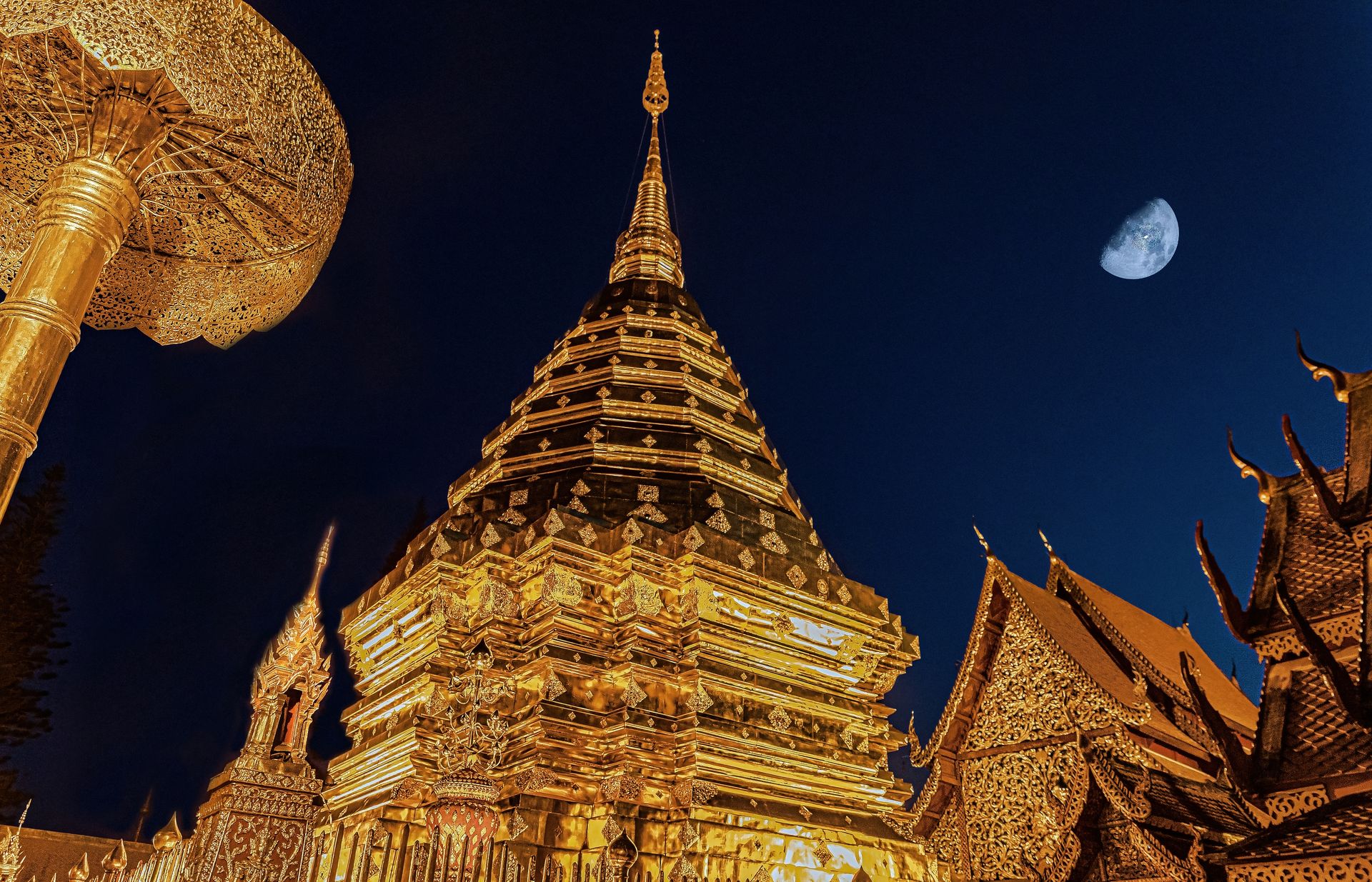 Golden Wat Phra That Doi Suthep pagoda illuminated at night with crescent moon.