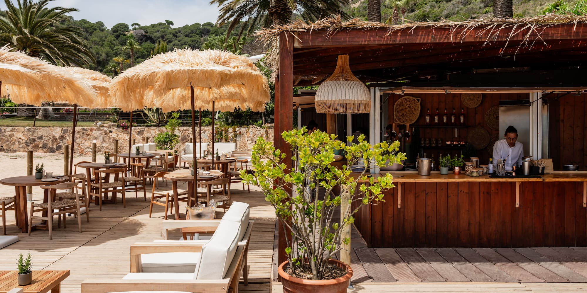 Beach bar deck with straw umbrellas, outdoor seating, and palm trees.