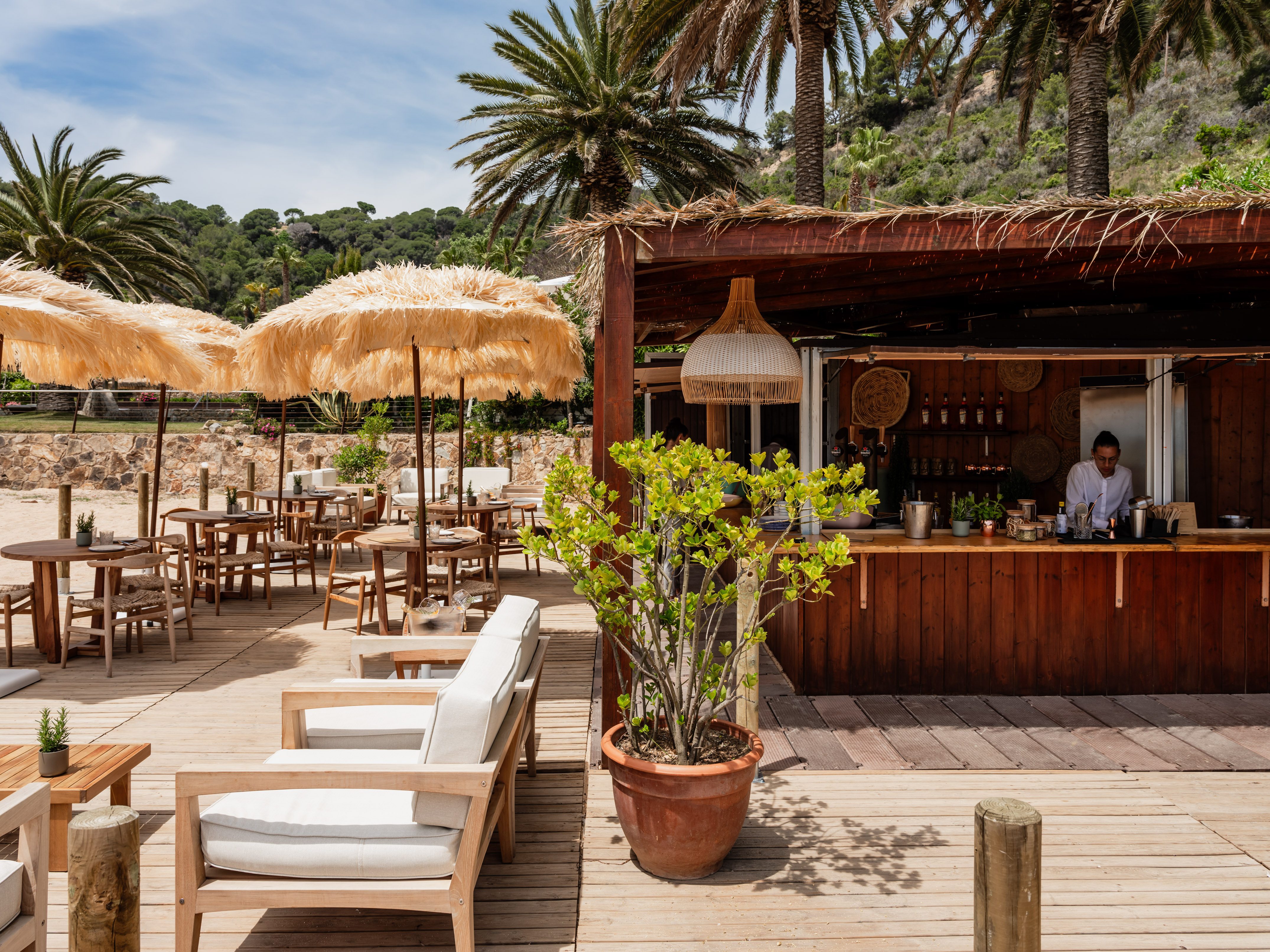 Beach bar deck with straw umbrellas, outdoor seating, and palm trees.