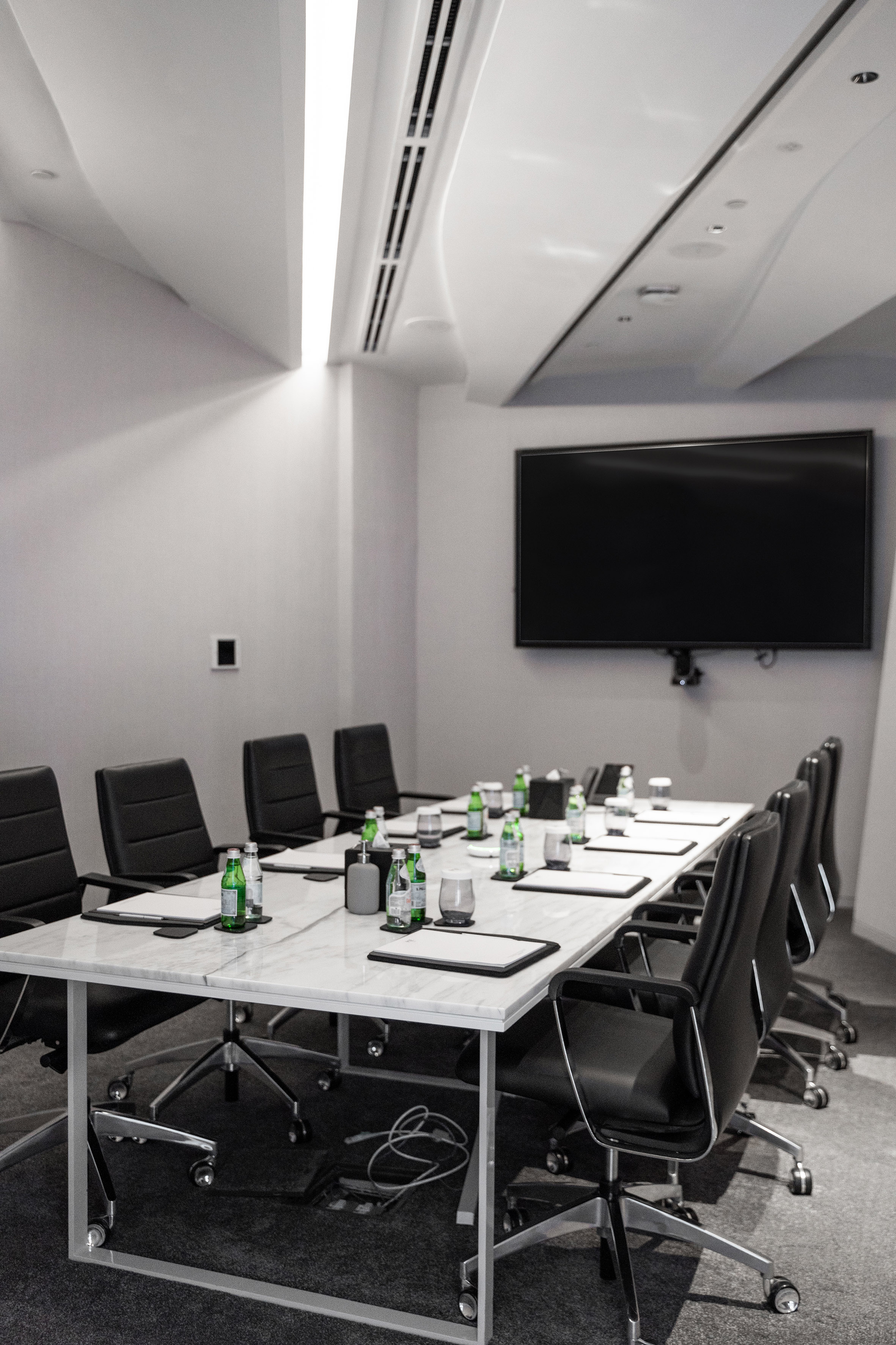 Modern conference room with marble table, black chairs, and large TV screen.