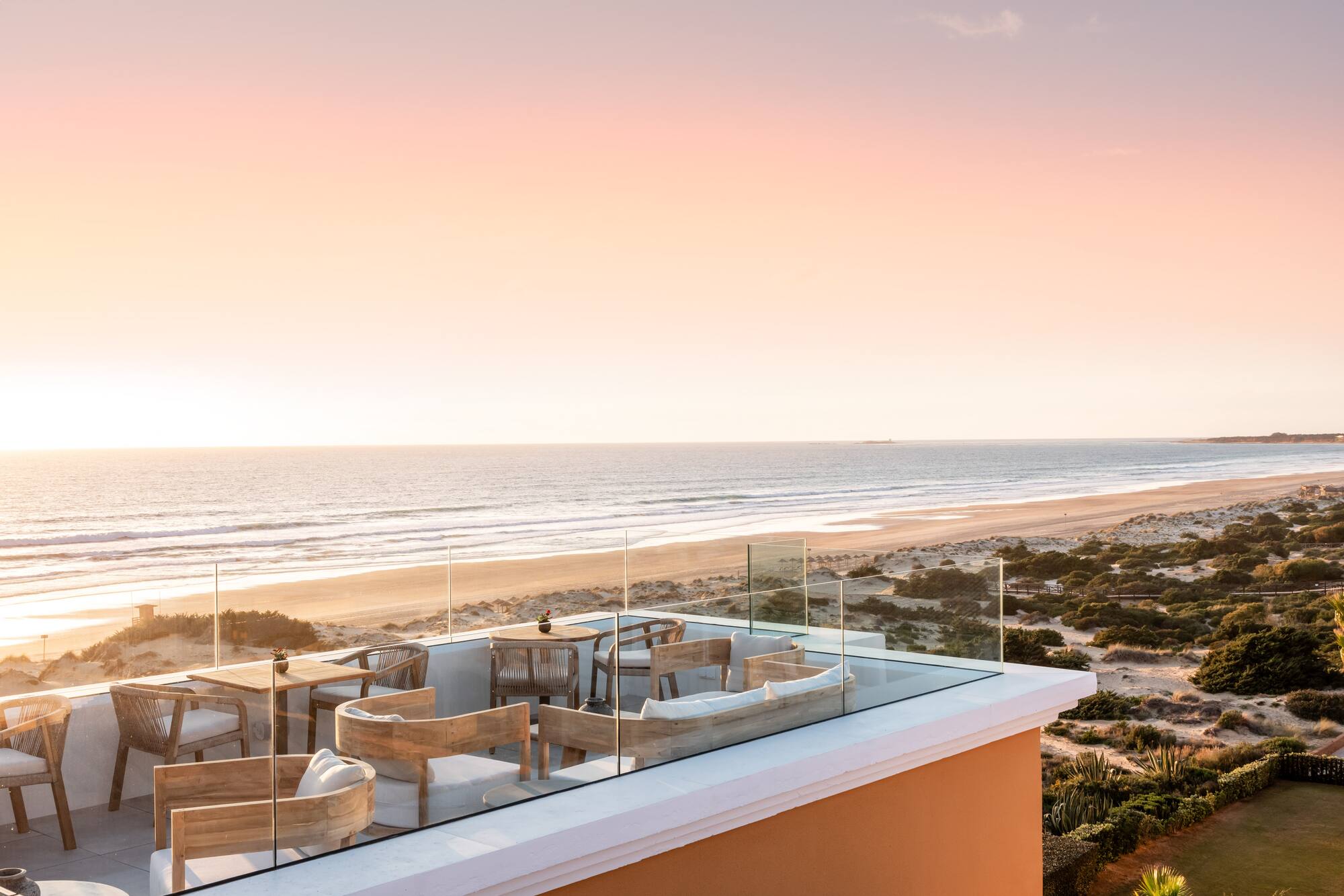Coastal rooftop terrace with outdoor seating, ocean, beach, and sunset.