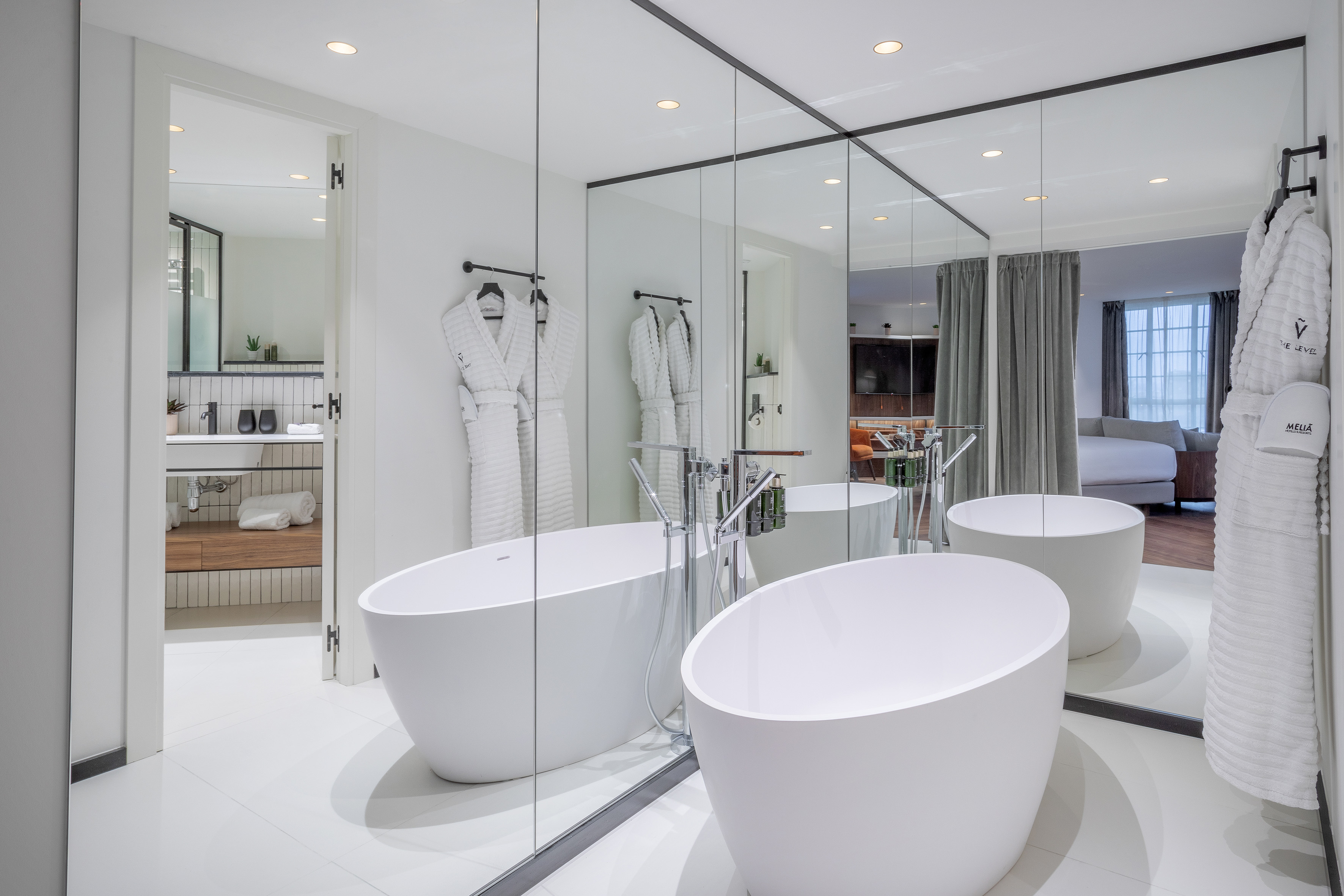 Luxury hotel suite bathroom with freestanding tub, bathrobes, and mirrored walls.