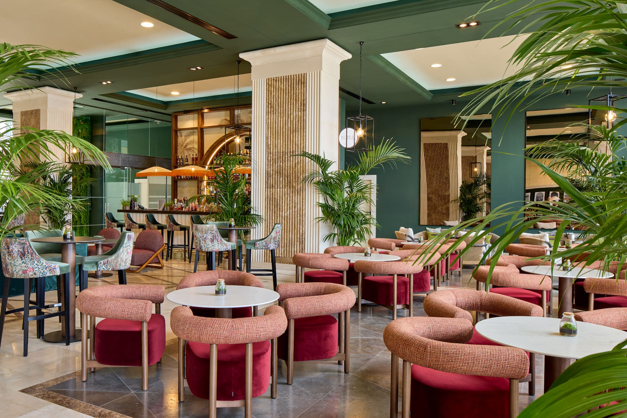Contemporary hotel bar lounge with green walls, palm plants, and stylish red seating.