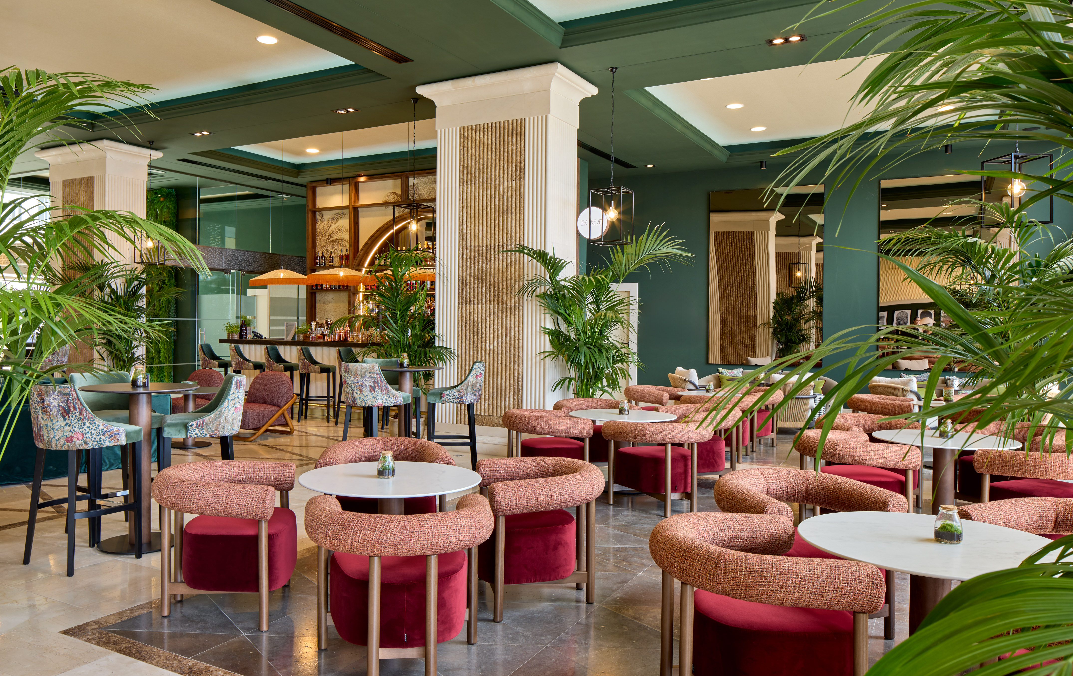 Contemporary hotel bar lounge with green walls, palm plants, and stylish red seating.