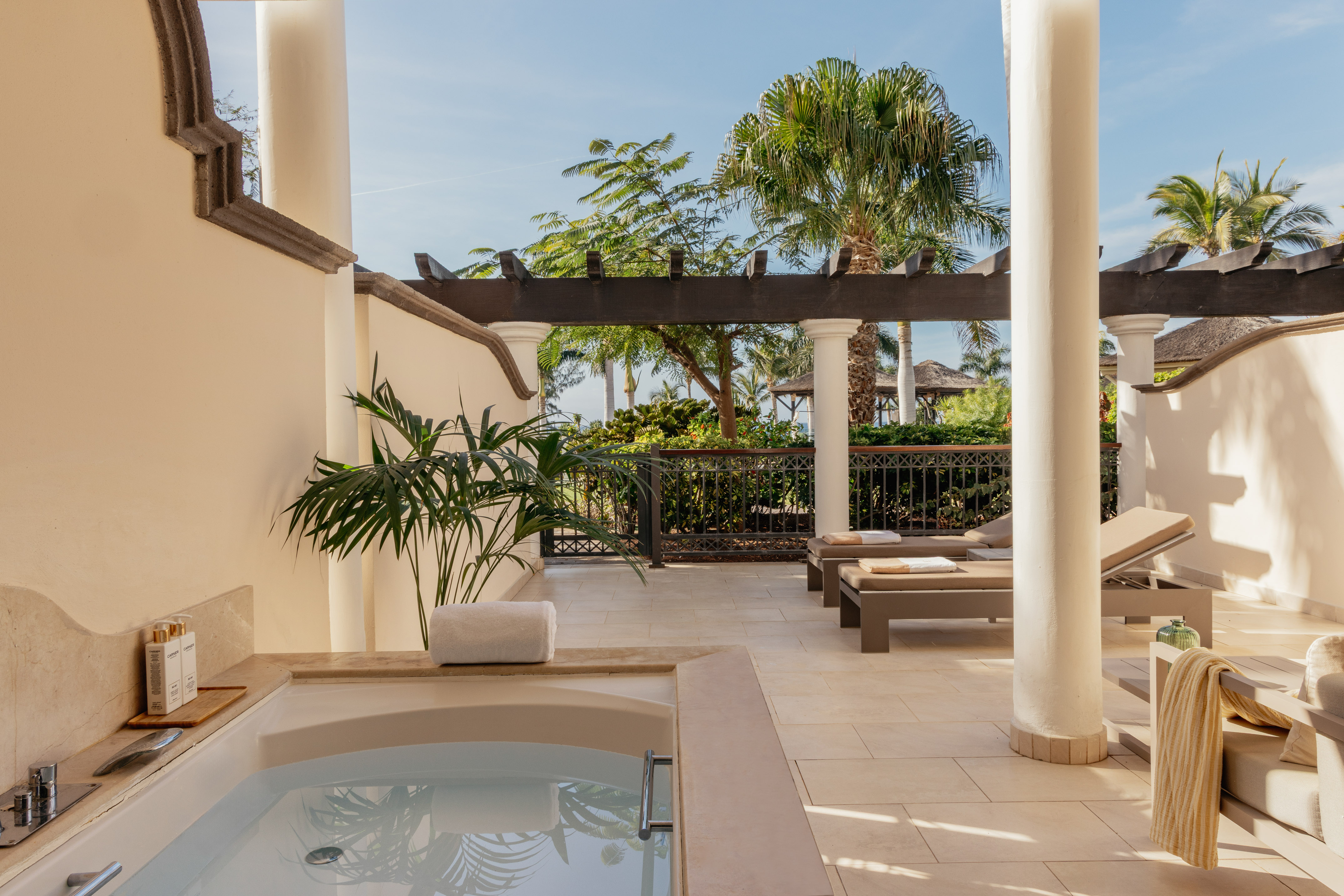 Private patio with outdoor soaking tub, sunbeds, and tropical landscaping.