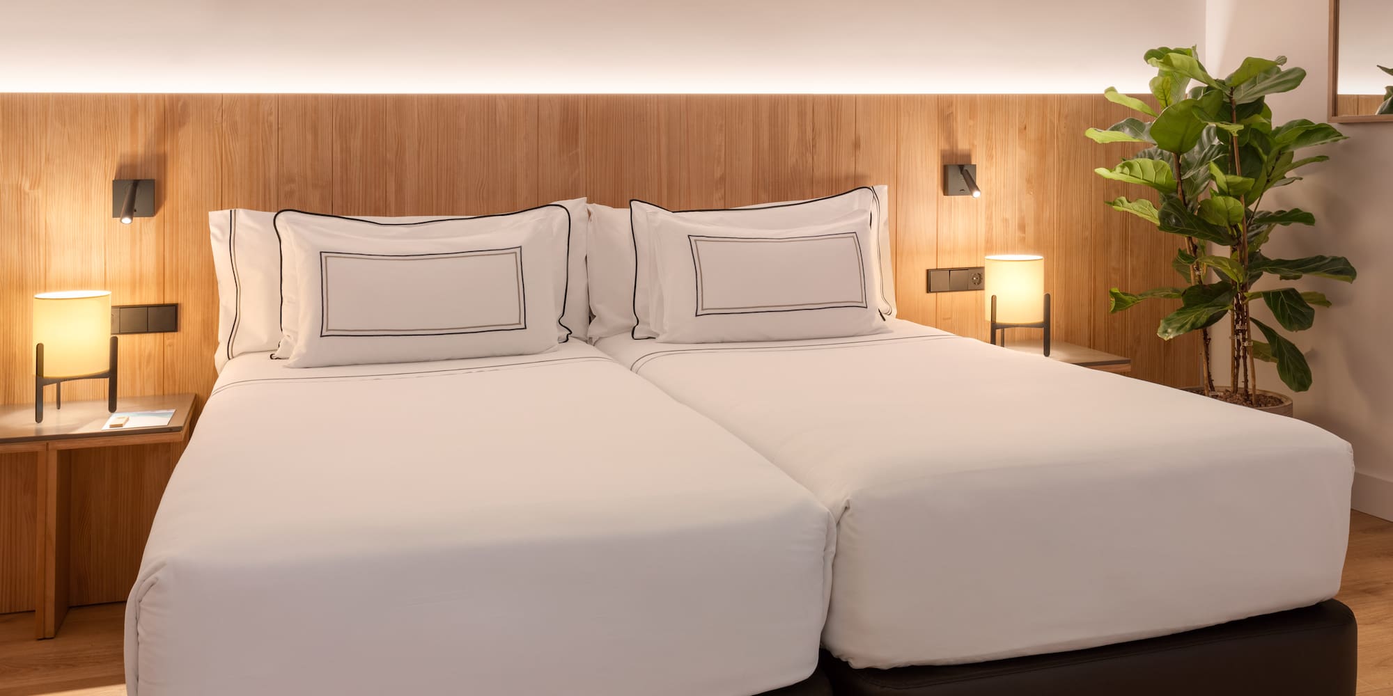 a bed with white sheets and a plant in front of it