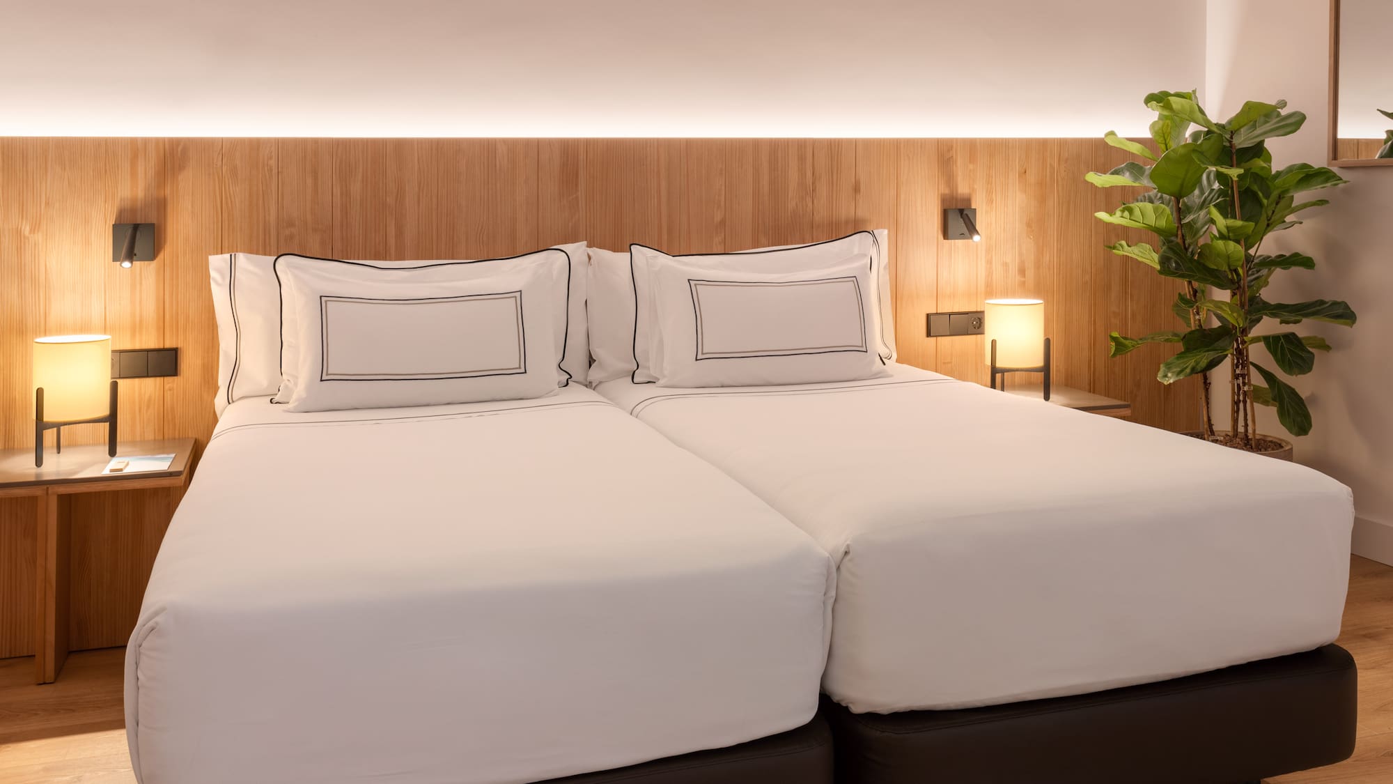 a bed with white sheets and a plant in front of it