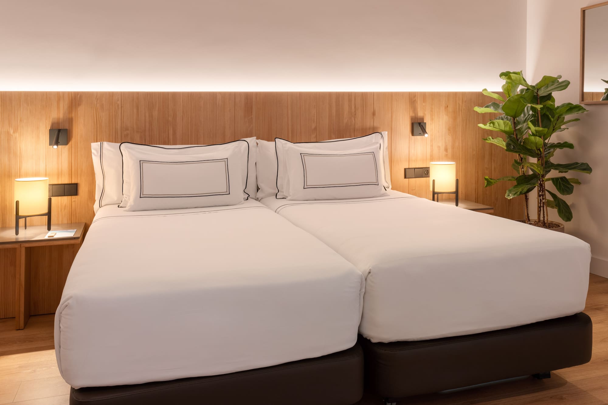 a bed with white sheets and a plant in front of it