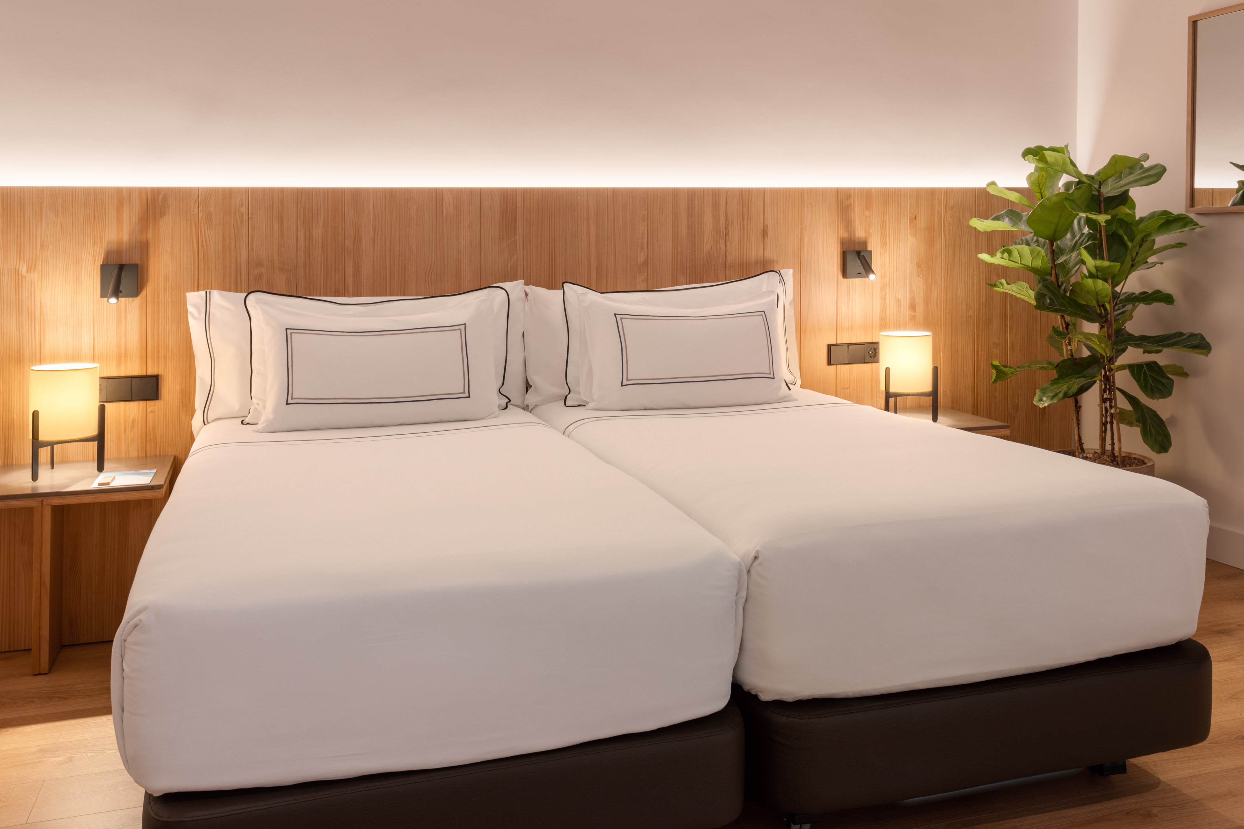 Hotel bedroom with two single beds, white linens, wooden headboard, and lamps.