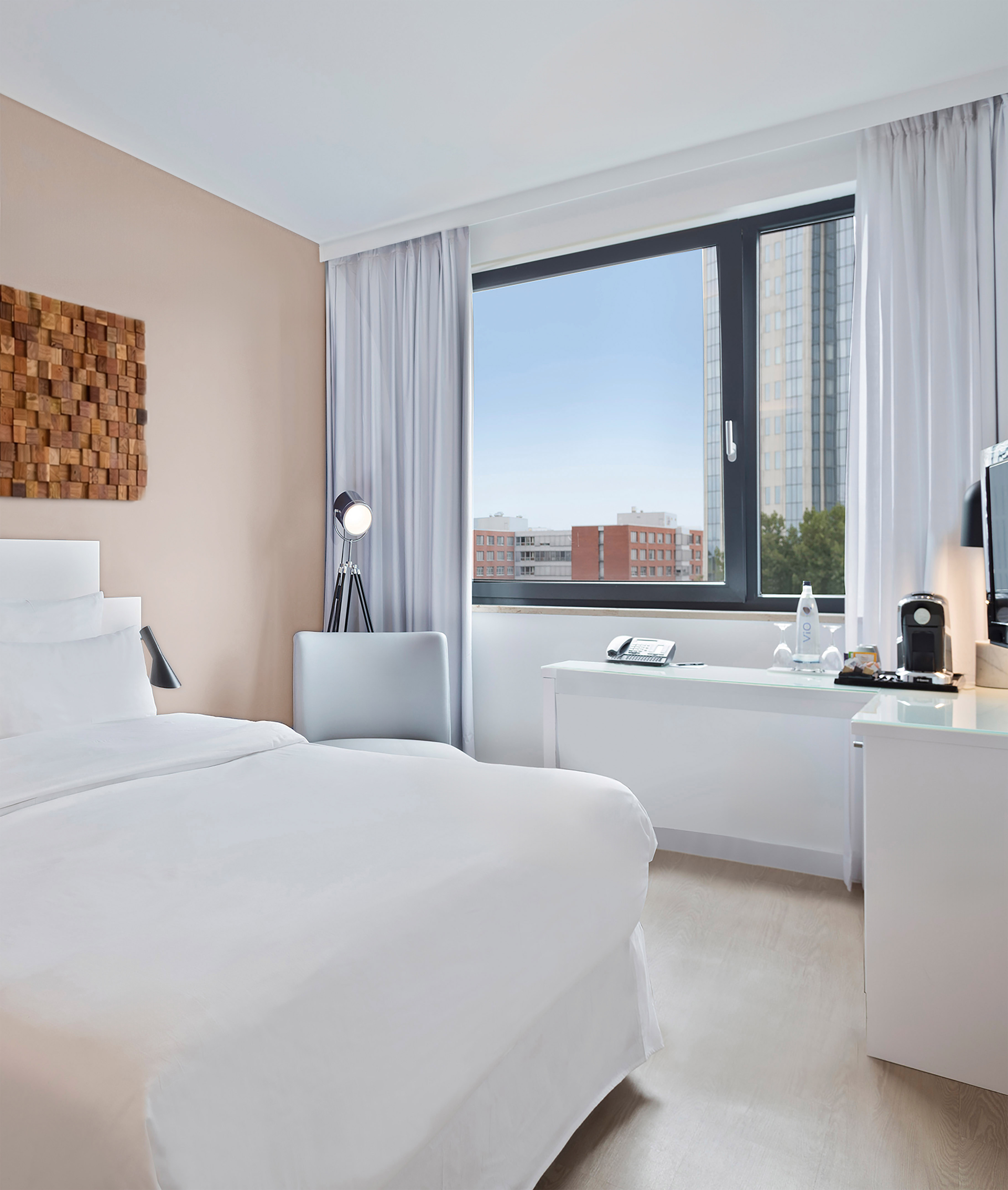 Clean, modern hotel room with white bed, large window, and cityscape view.