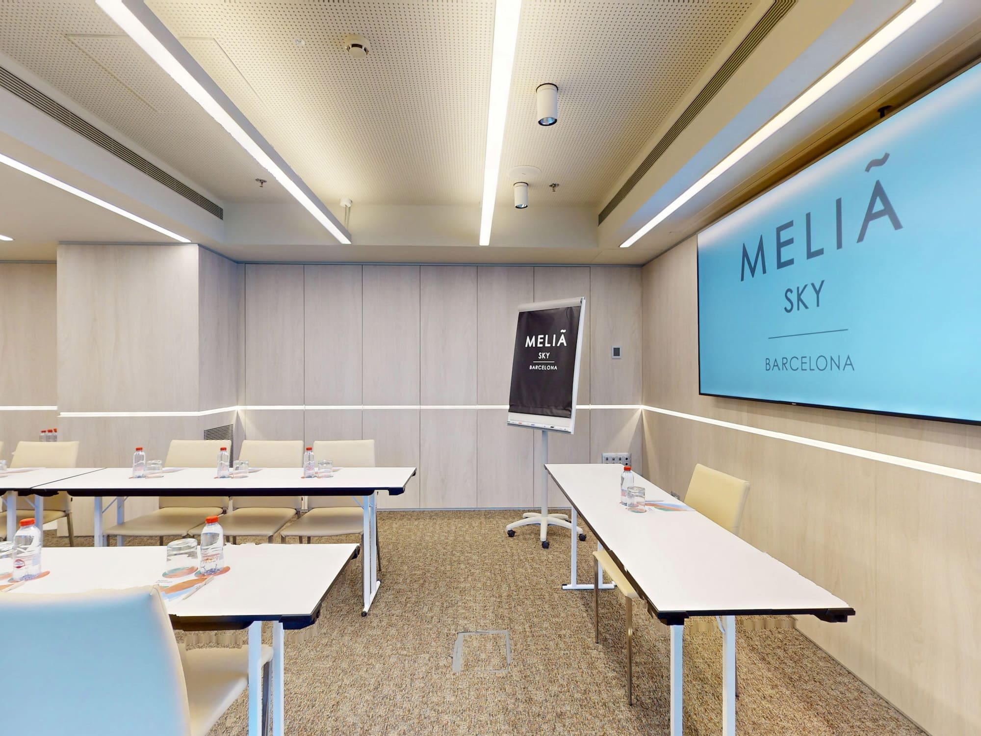 Modern Meliá Sky Barcelona conference room with screen, tables, and flip chart.