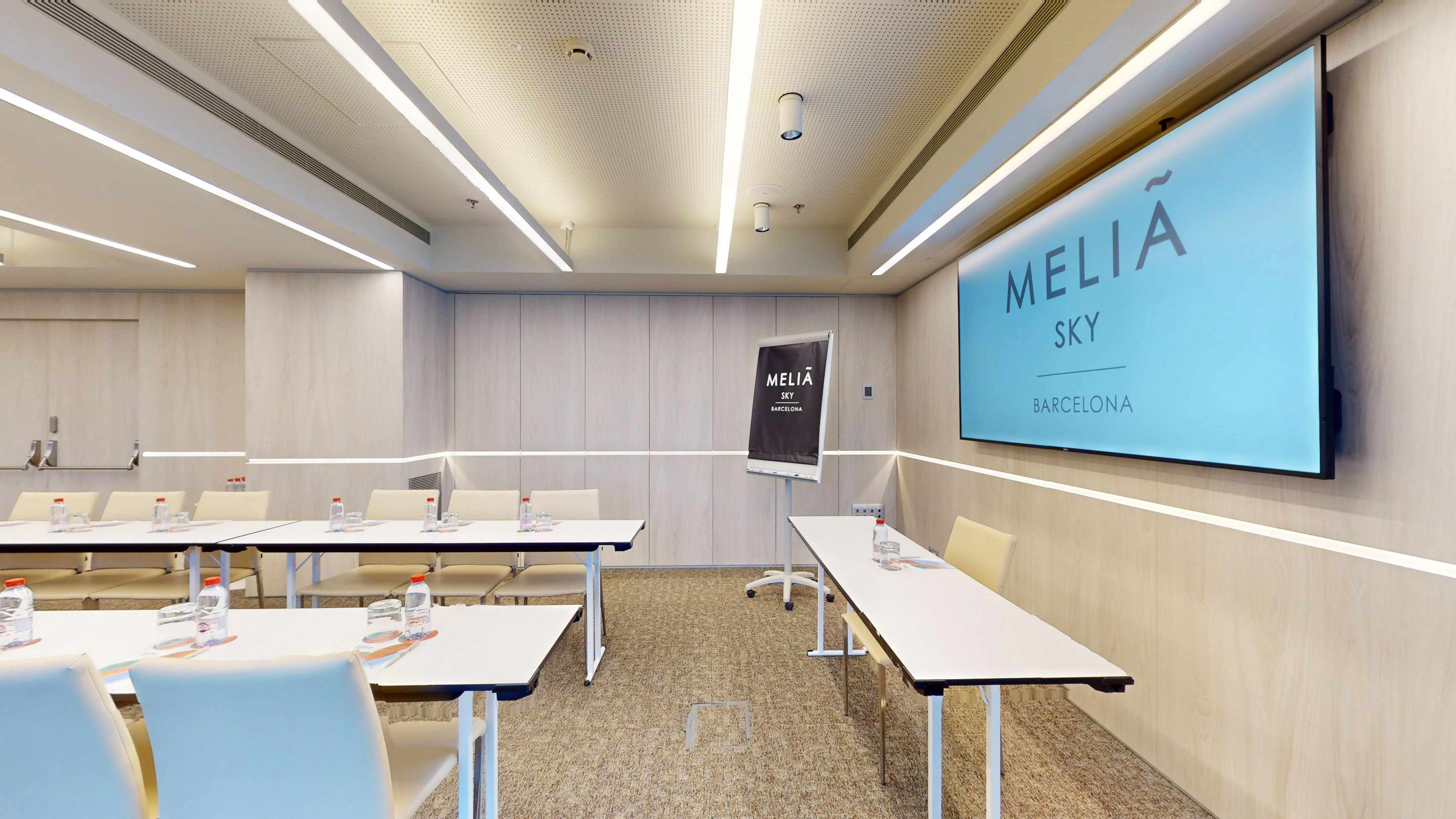 Modern Meliá Sky Barcelona conference room with screen, tables, and flip chart.