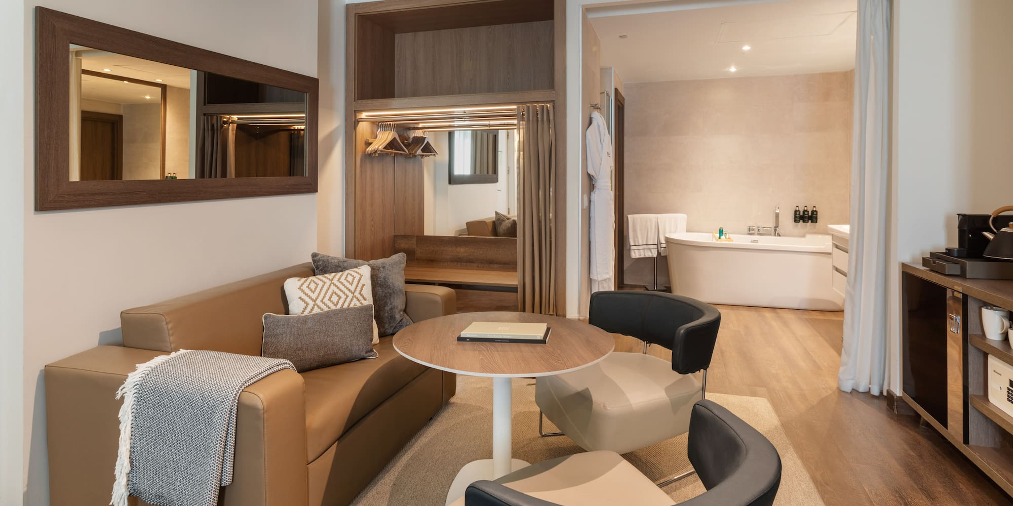 Hotel suite living area with sofa, coffee table, and view to modern bathtub.