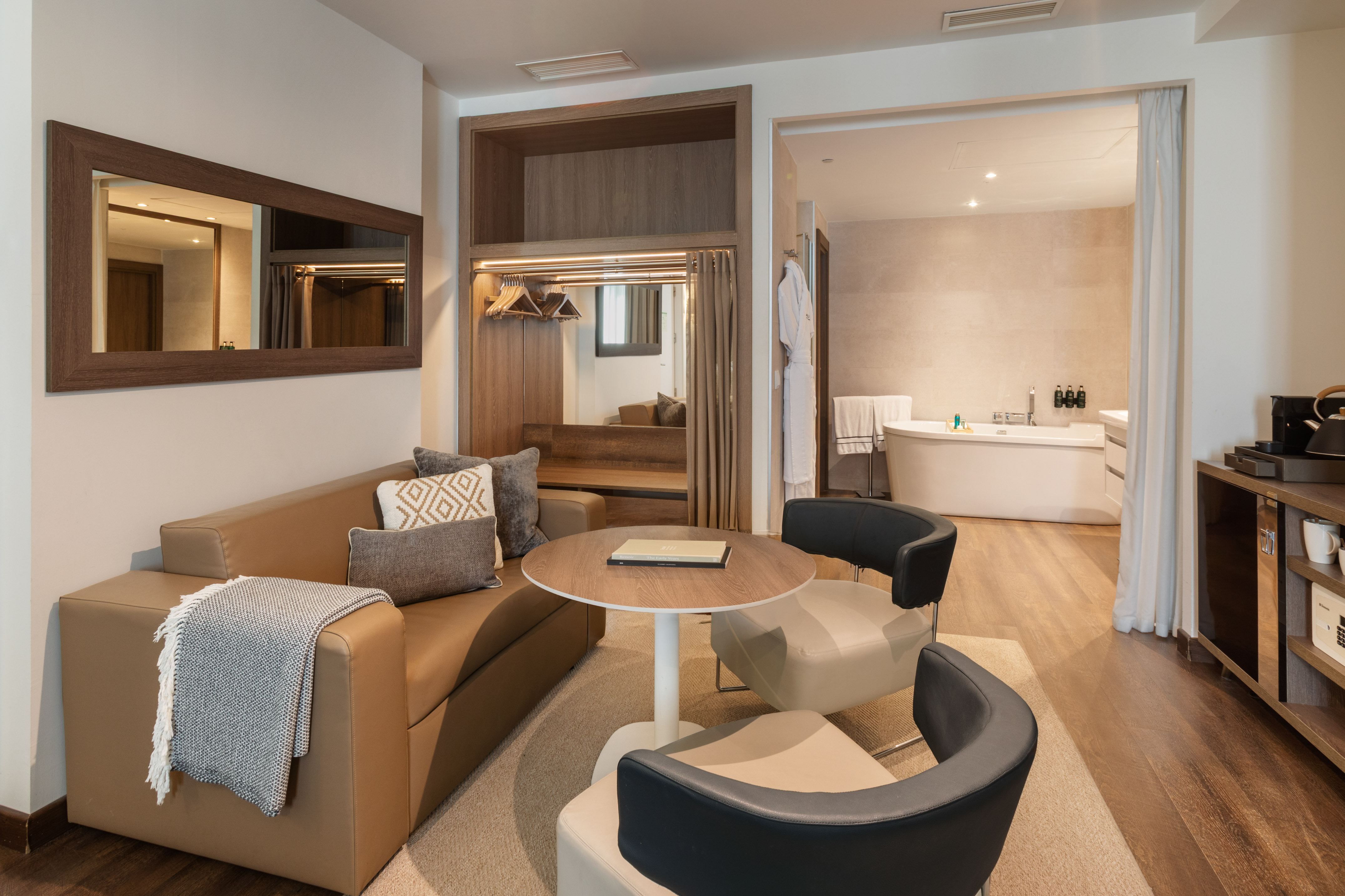 Hotel suite living area with sofa, coffee table, and view to modern bathtub.