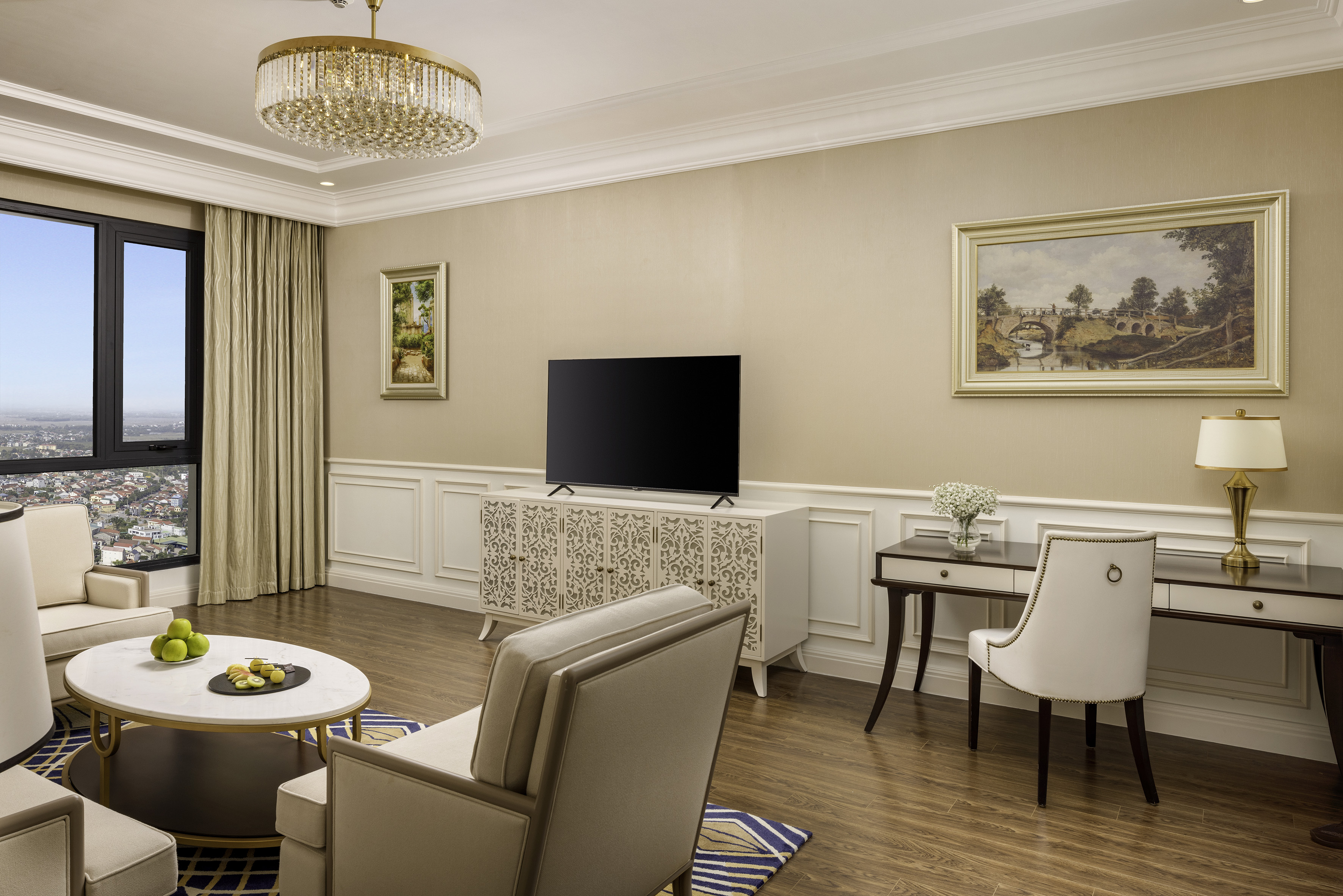 Elegant living room with city view, modern TV, plush seating, and desk area.