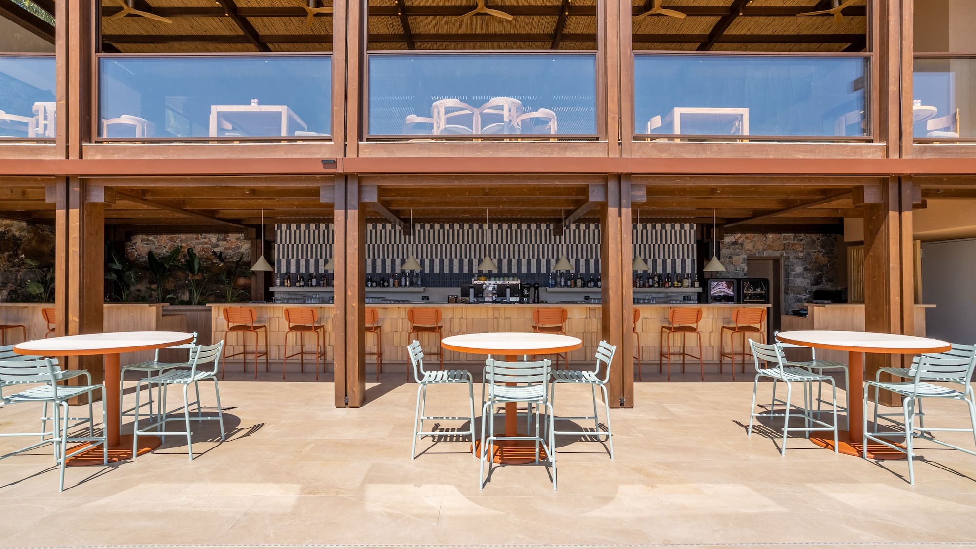 Outdoor resort bar with light blue chairs, orange bar stools, and bamboo ceiling.