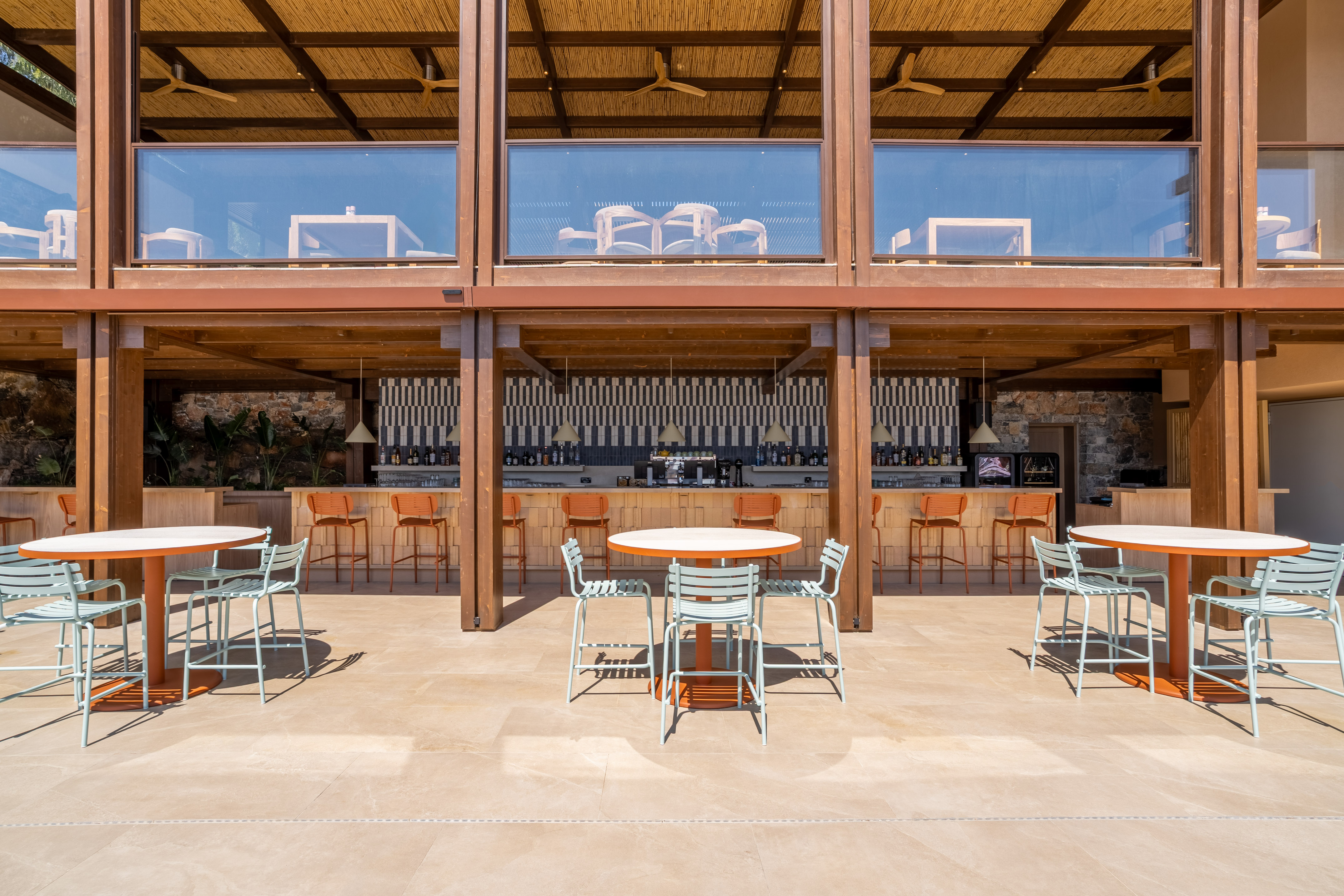 Outdoor resort bar with light blue chairs, orange bar stools, and bamboo ceiling.