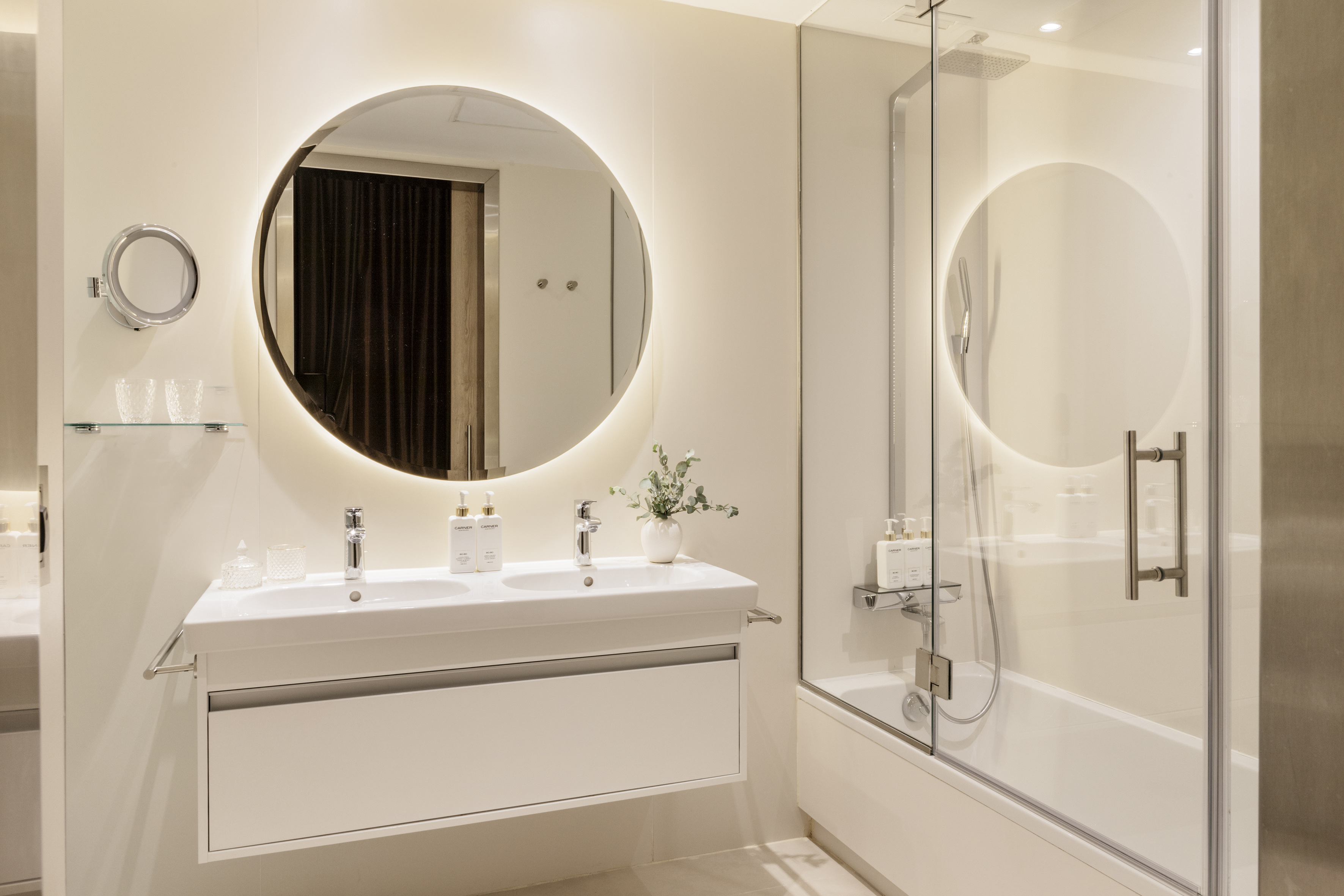Modern white bathroom with double vanity, lighted mirror, and tub shower combo.