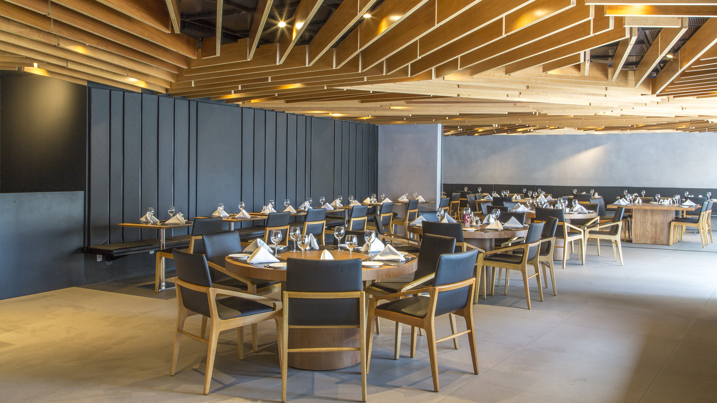 Modern dining room with wooden ceiling, dark walls, and set tables.