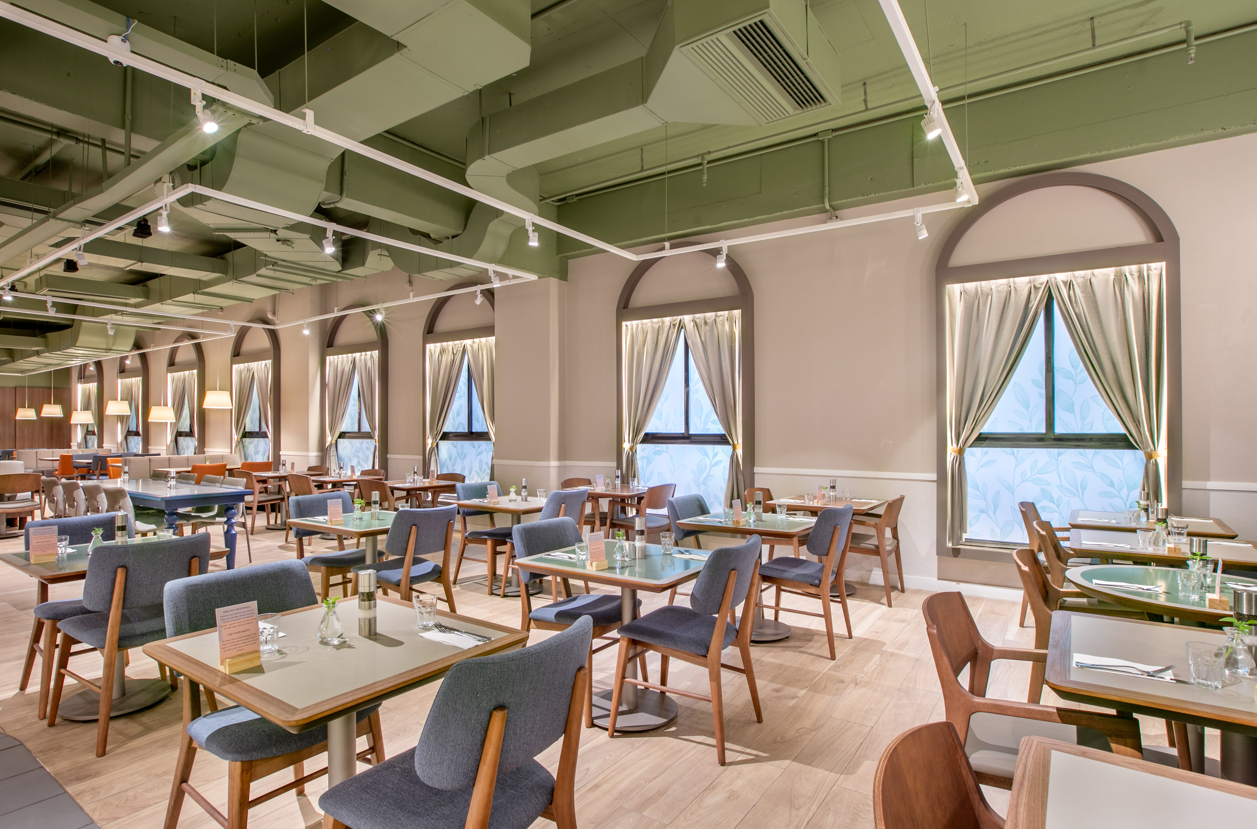 Restaurant dining area with modern furniture, green ceiling, and arched windows.