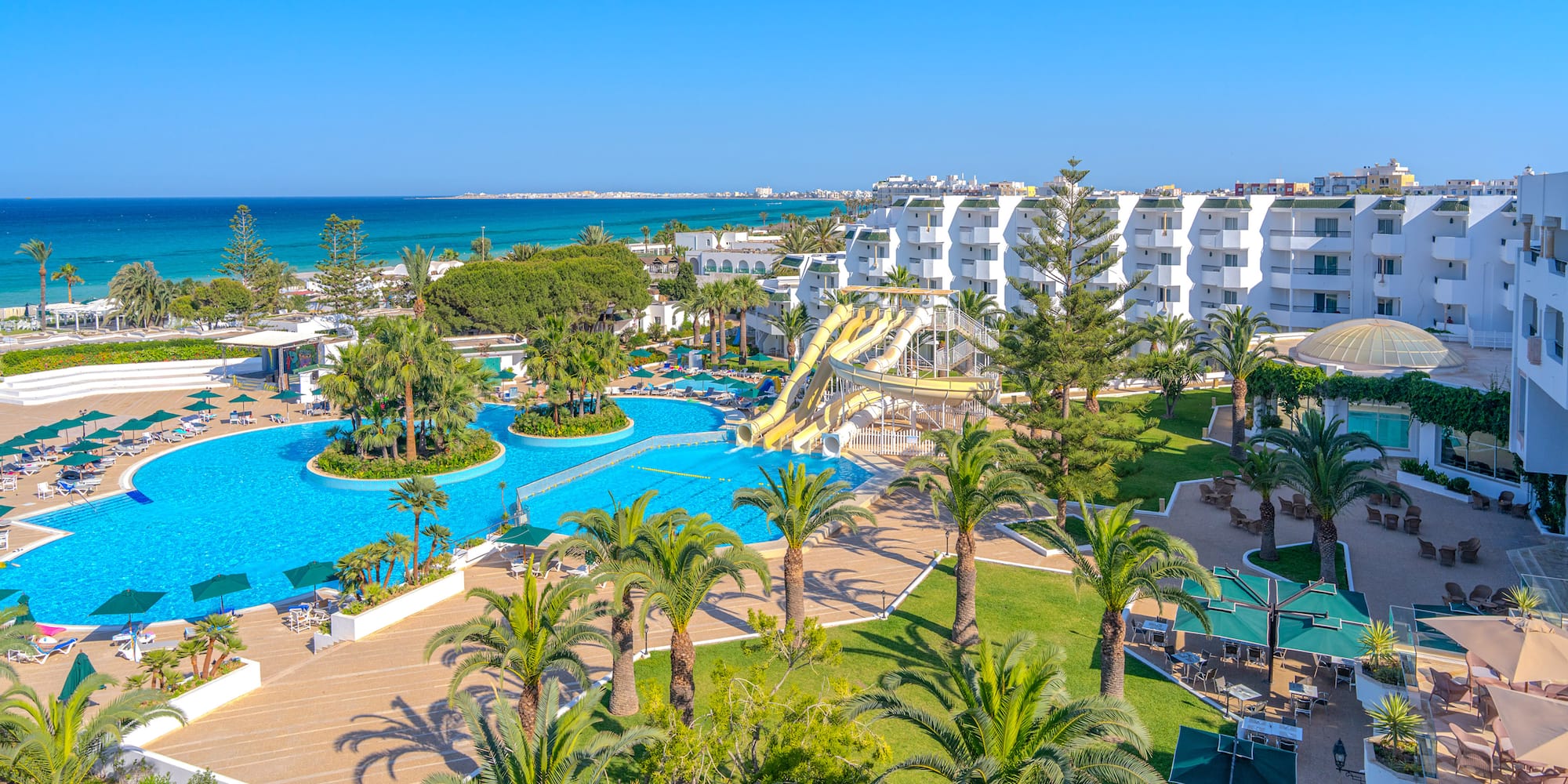 Coastal resort with big pools, water slides, palm trees, and ocean.
