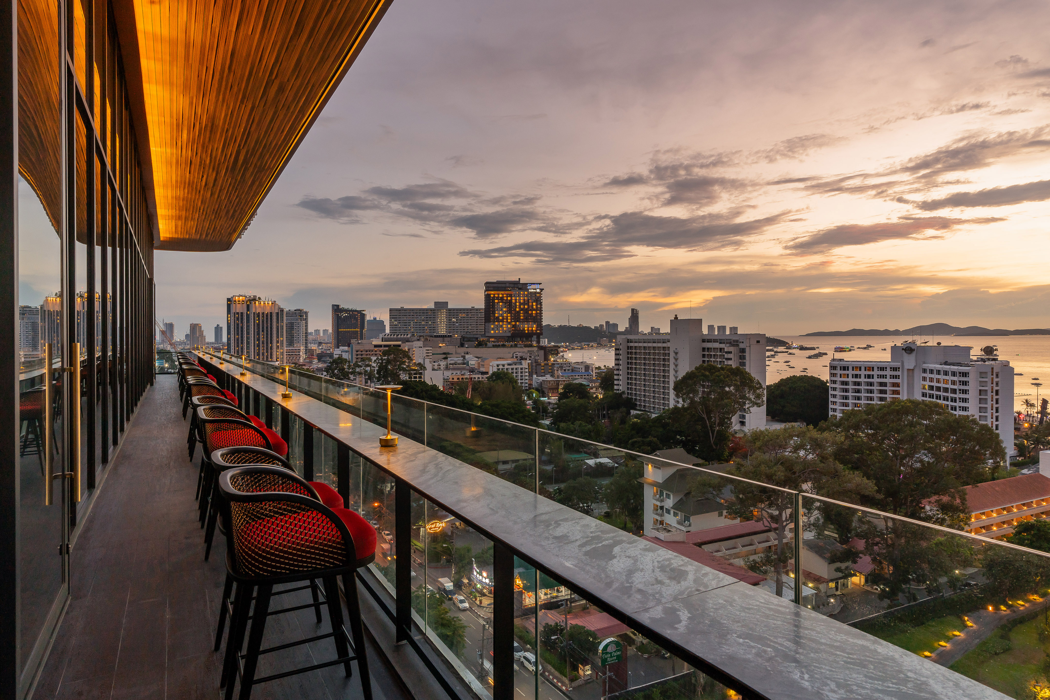 Modern rooftop bar overlooking Pattaya cityscape and ocean at sunset.