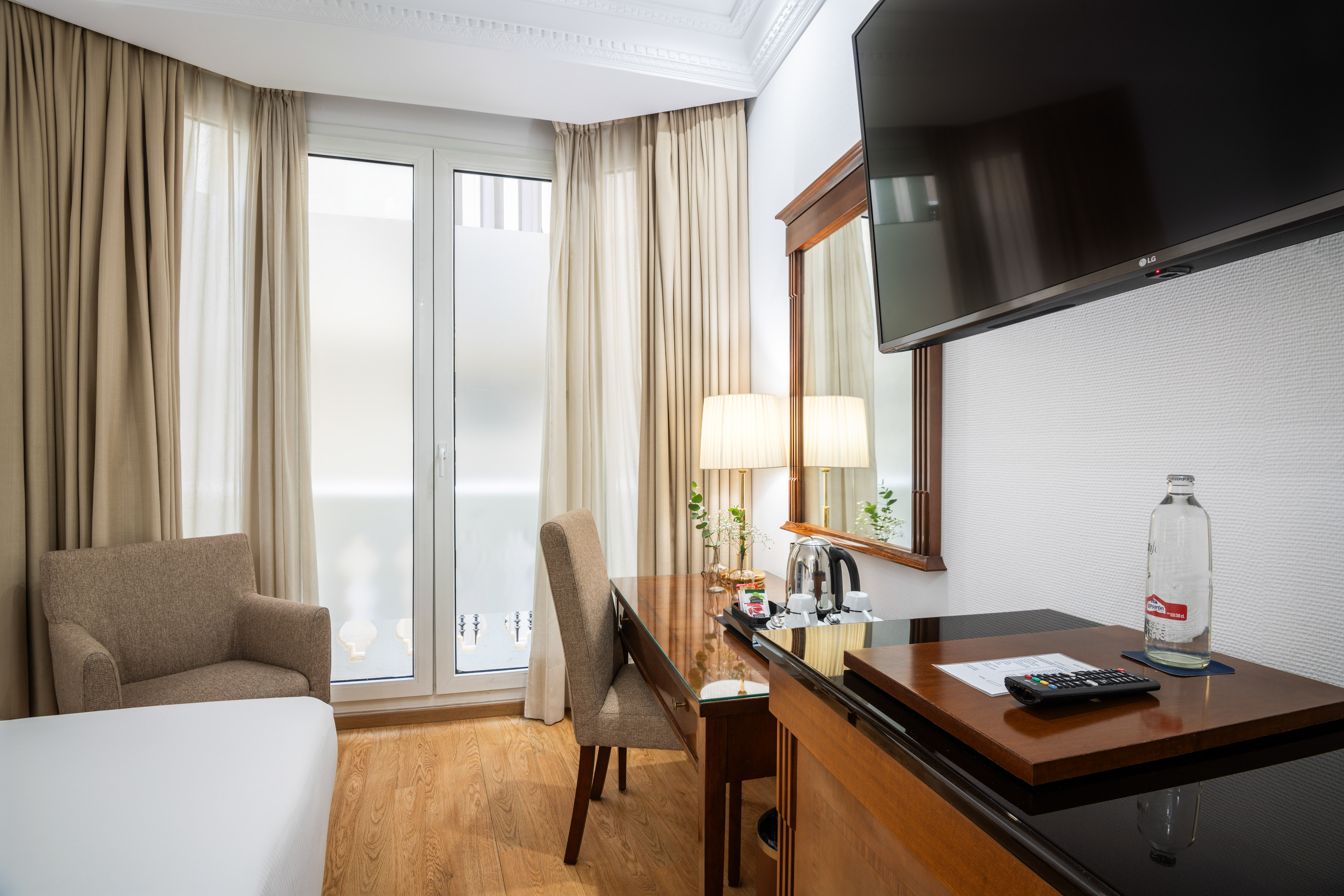 Hotel room with desk, chair, flat-screen TV, and large window with curtains.