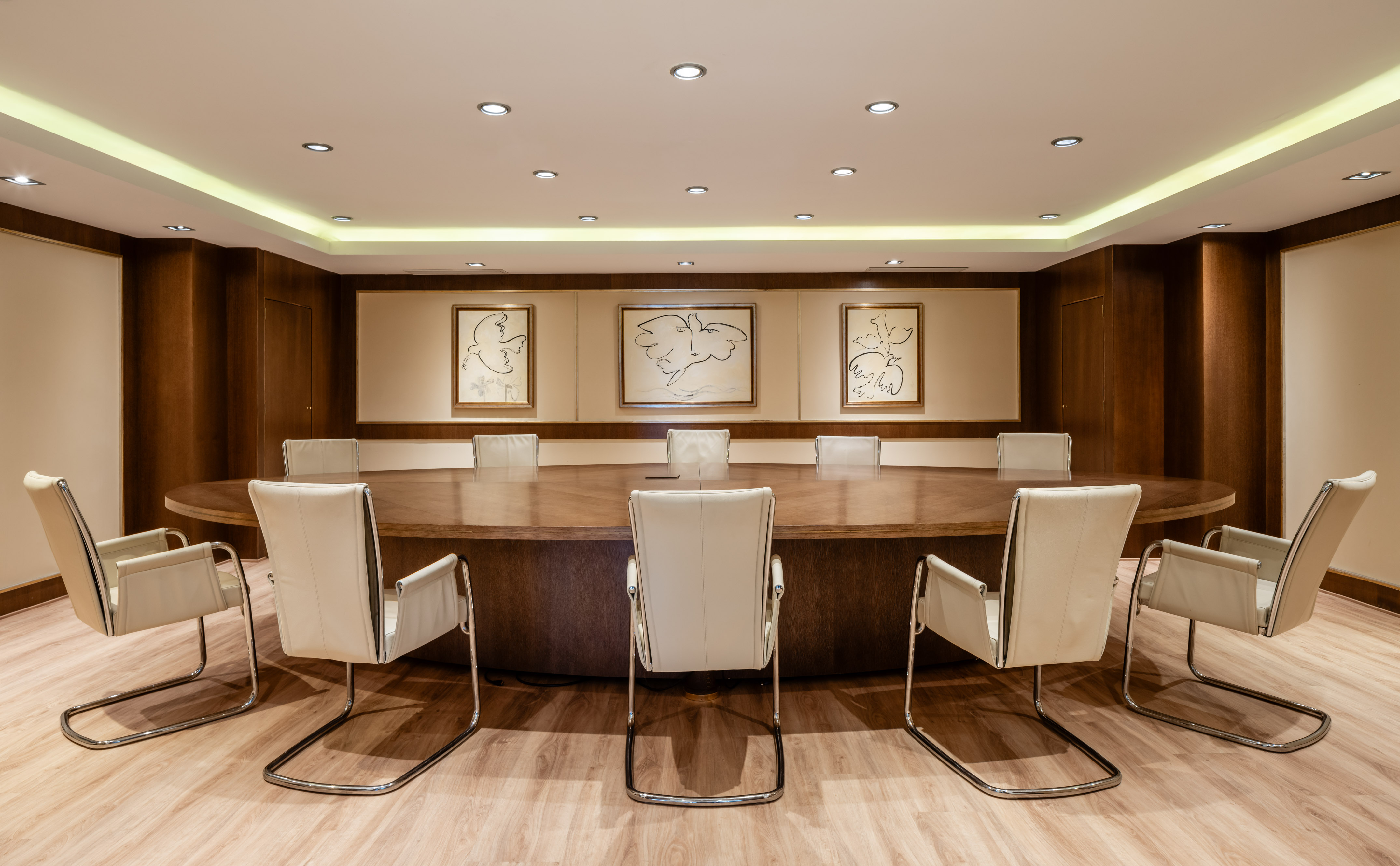 Modern boardroom with oval wooden table, cream leather chairs, and abstract art.