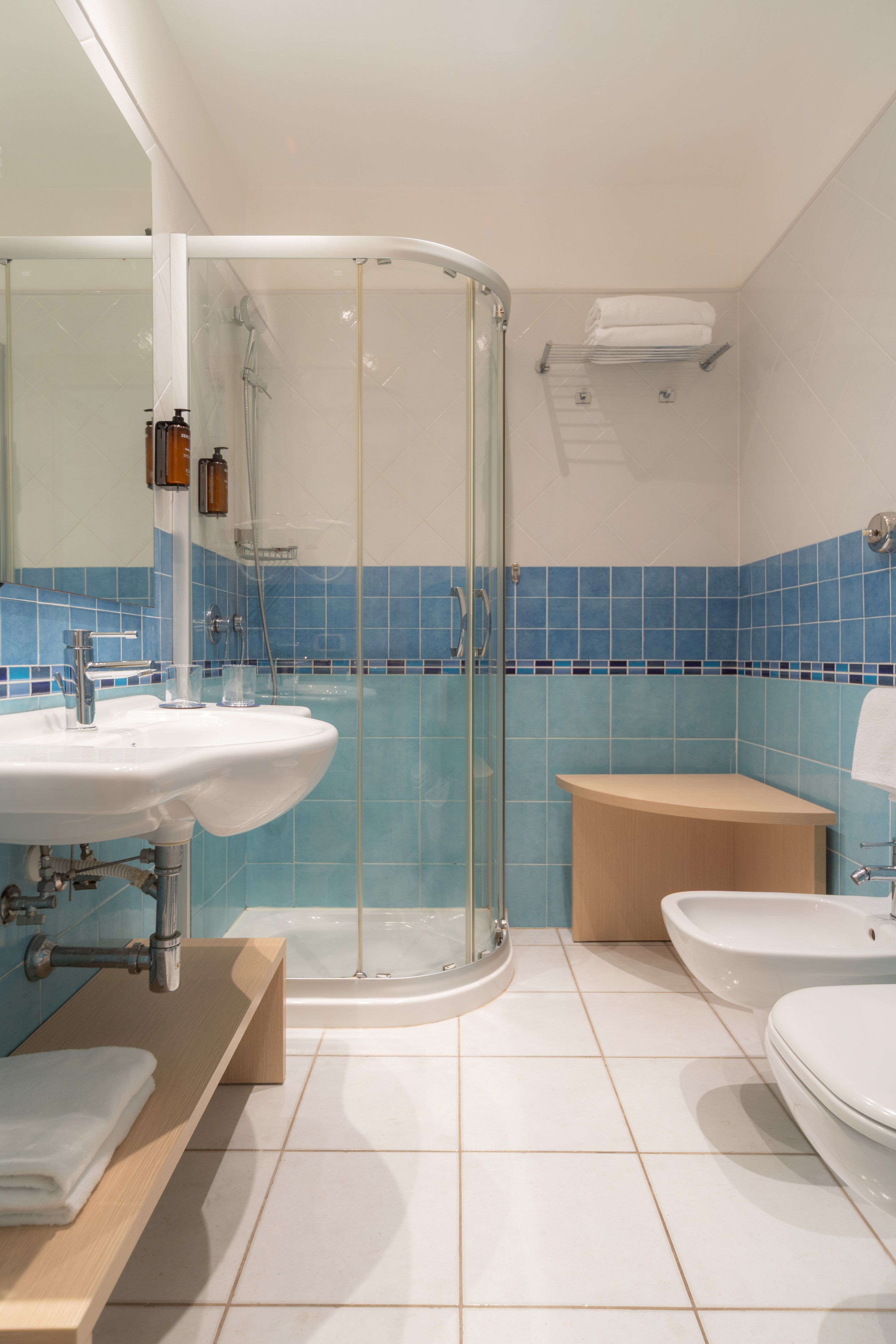 Blue and white tiled bathroom with glass shower, sink, toilet, and bidet.