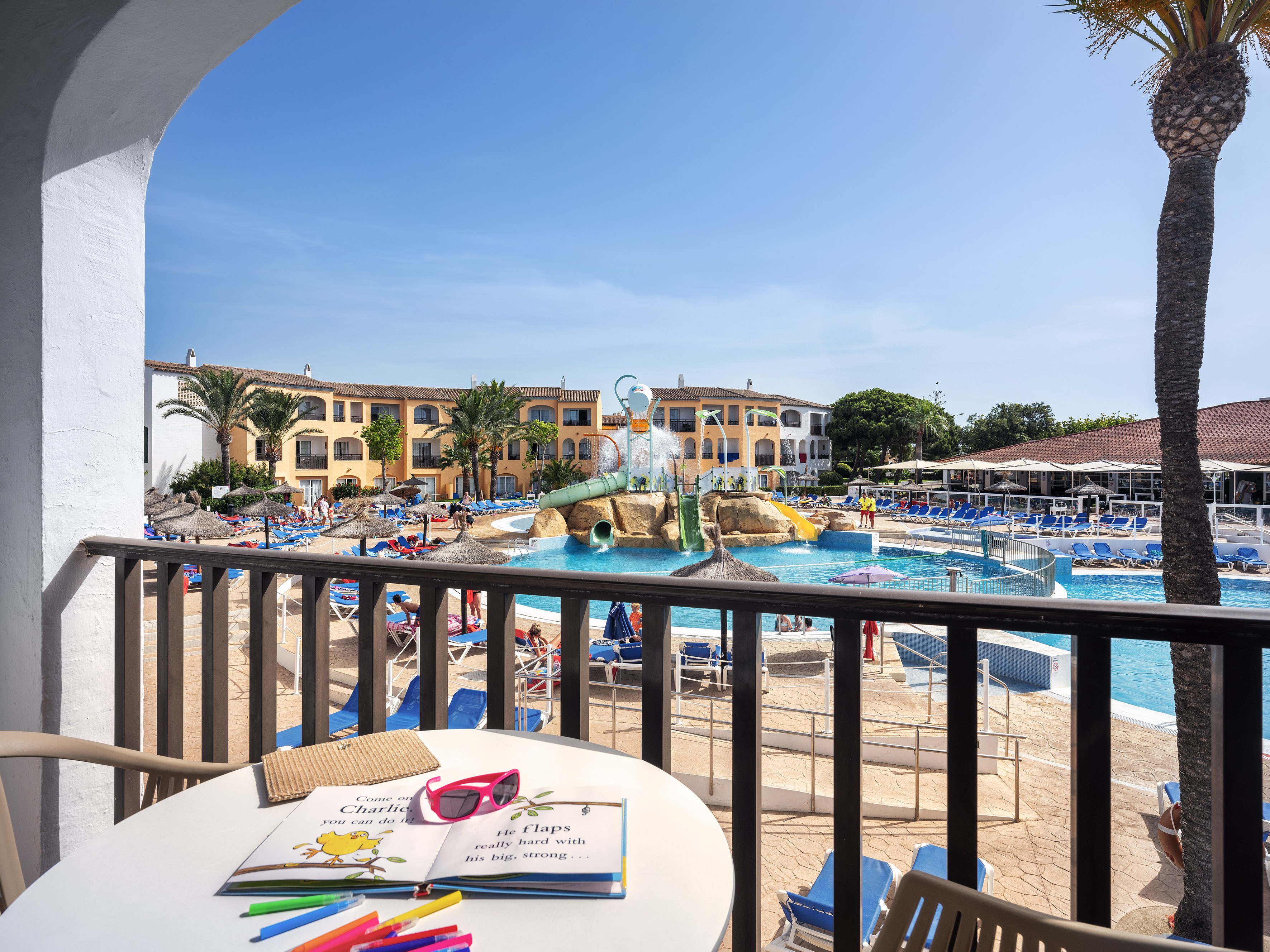 Family resort balcony with pool view, waterslides, and hotel buildings.