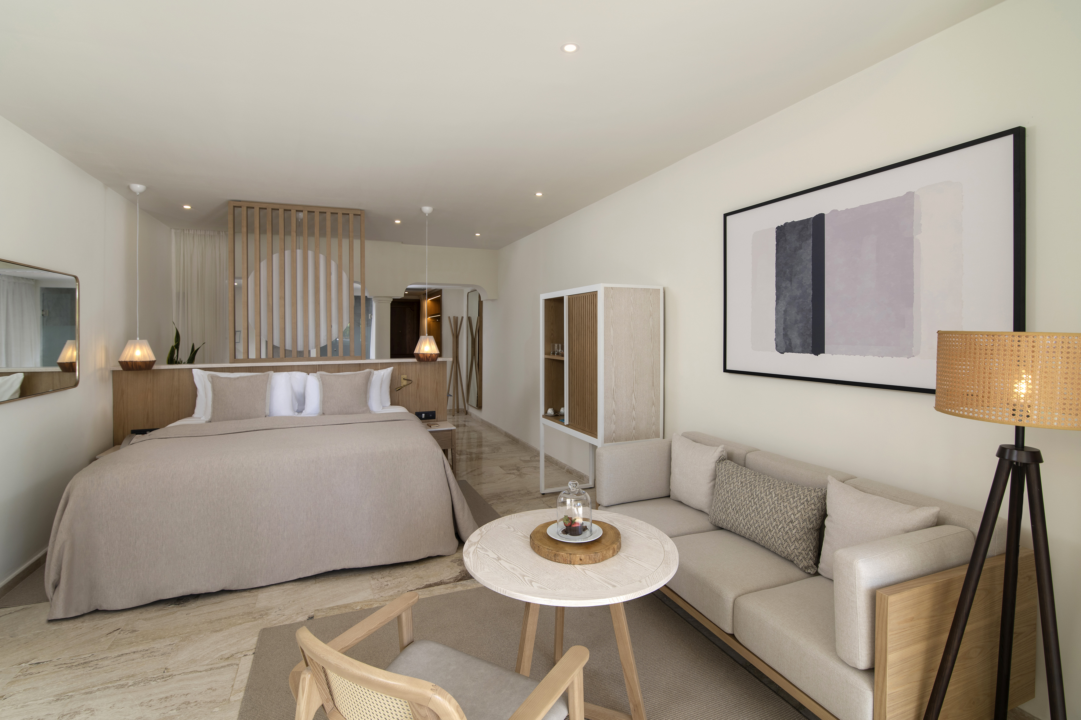 Modern hotel suite: large bed, neutral decor, comfortable sofa, abstract art.
