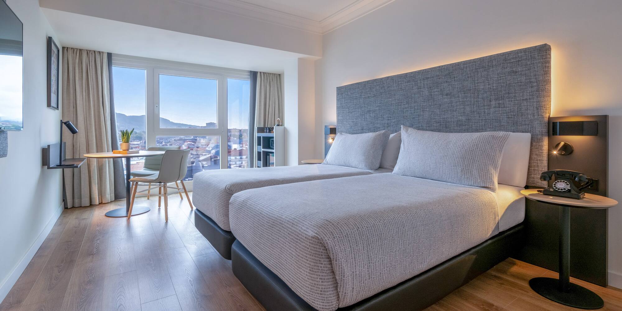 Habitación de hotel moderna con dos camas, vistas a la ciudad y suelo de madera.
