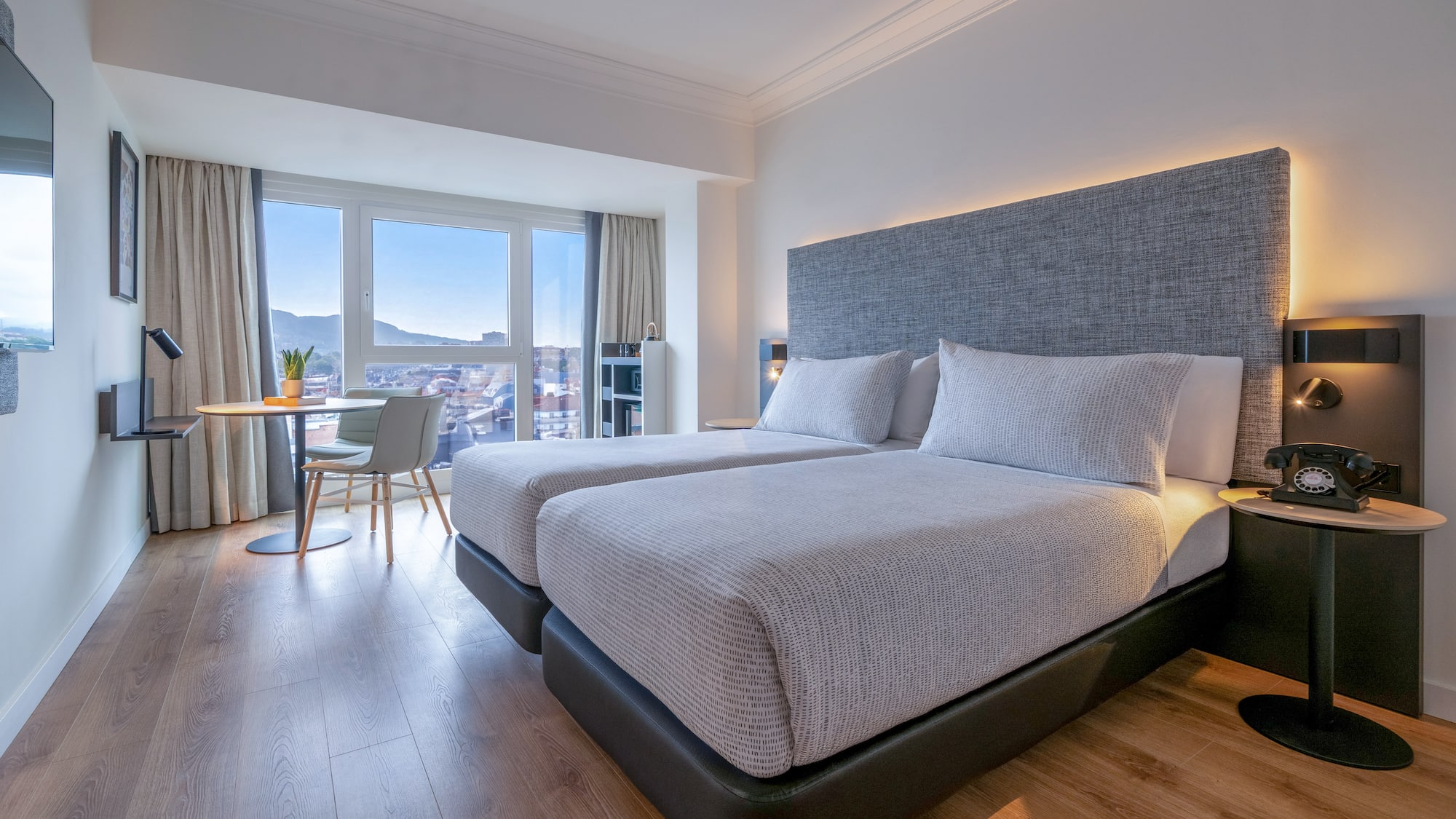 Habitación de hotel moderna con dos camas, vistas a la ciudad y suelo de madera.