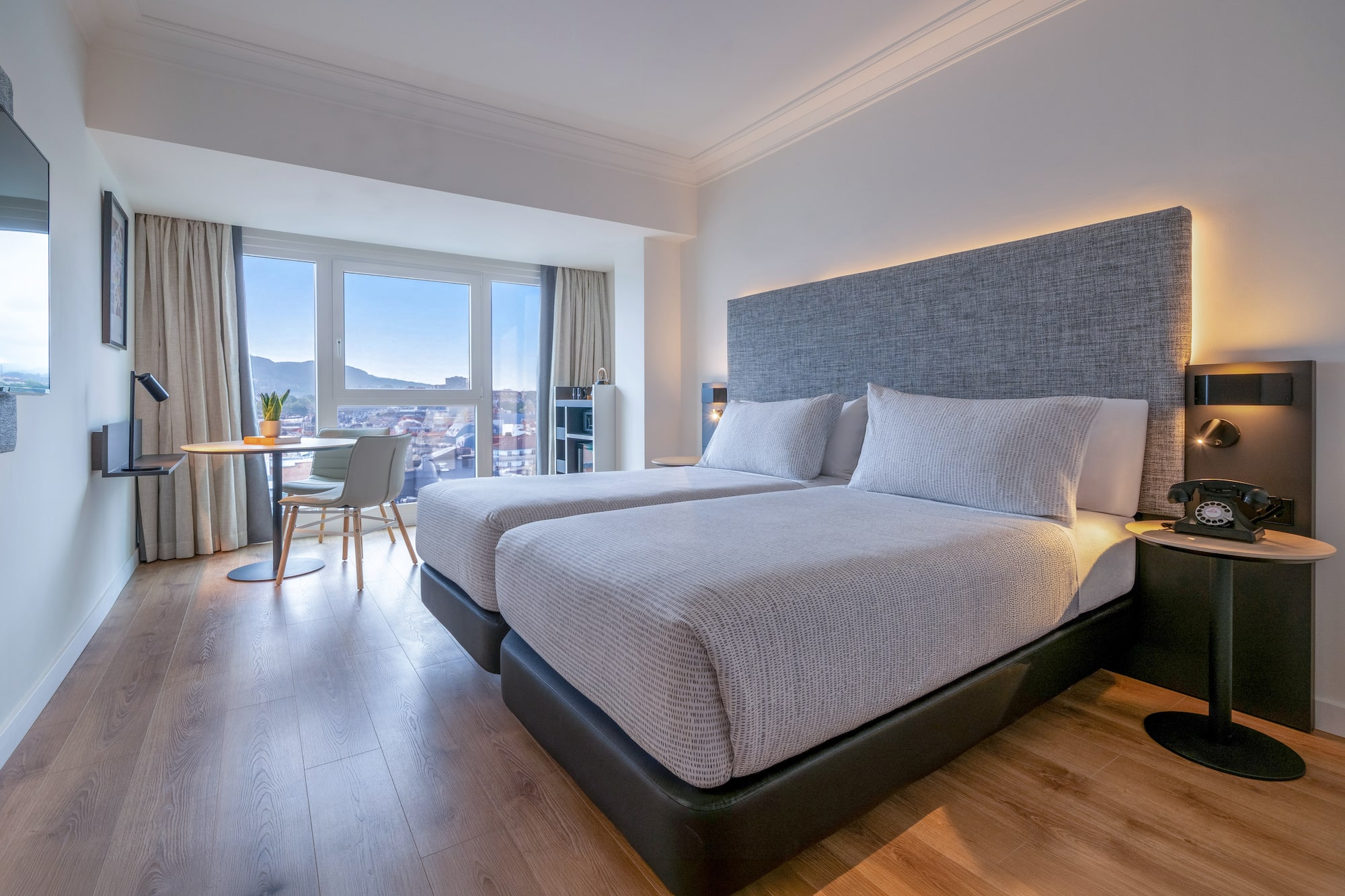 Habitación de hotel moderna con dos camas, vistas a la ciudad y suelo de madera.