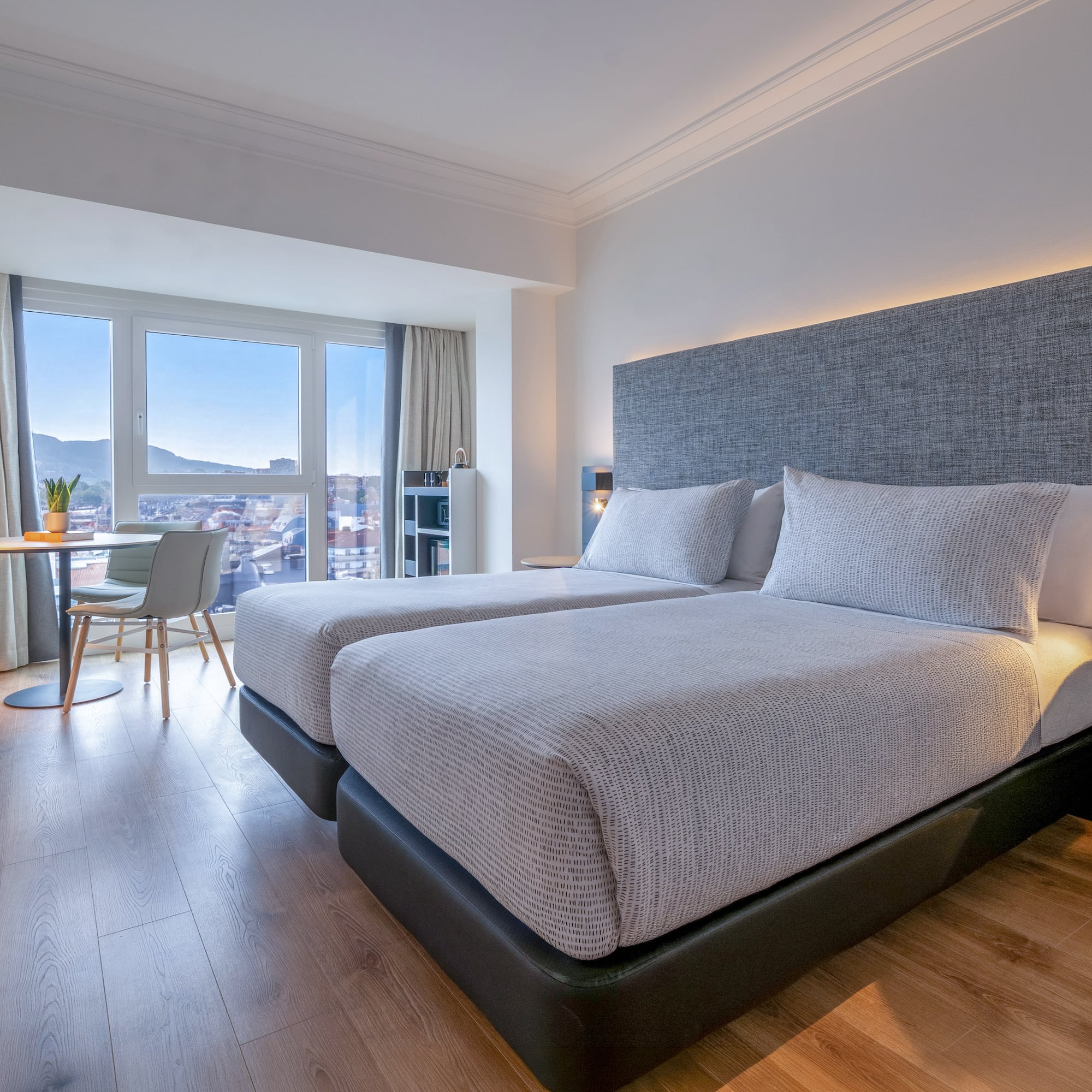 Habitación de hotel moderna con dos camas, vistas a la ciudad y suelo de madera.