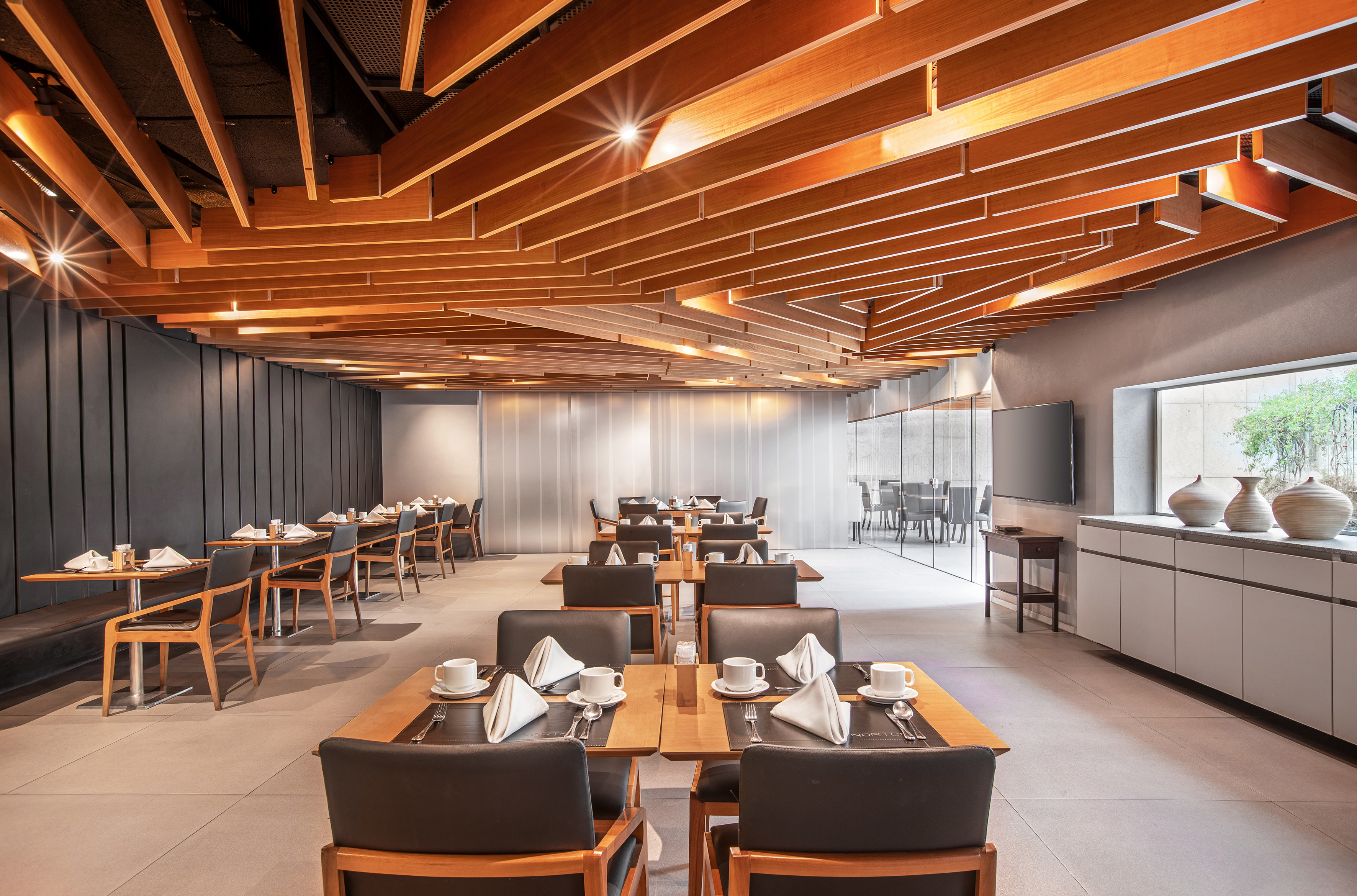 Modern restaurant dining room with stylish wooden slat ceiling and set tables.
